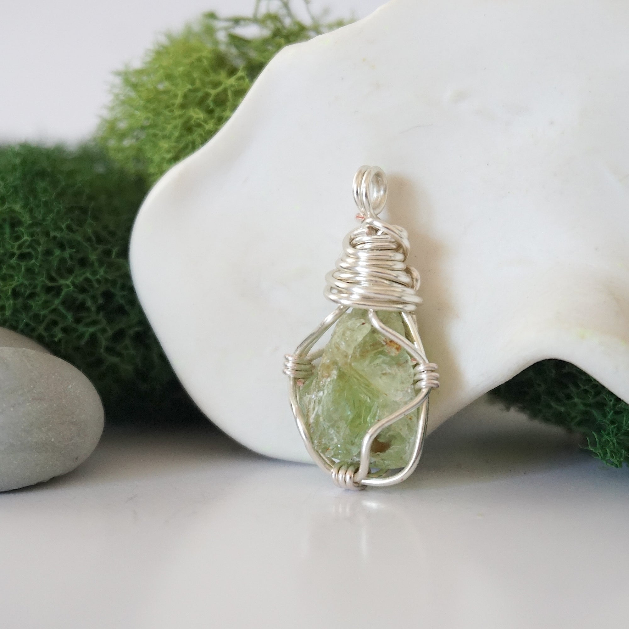 Detailed side angle view of simple raw peridot pendant in silver wire