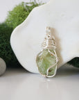 Detailed side angle view of simple raw peridot pendant in silver wire
