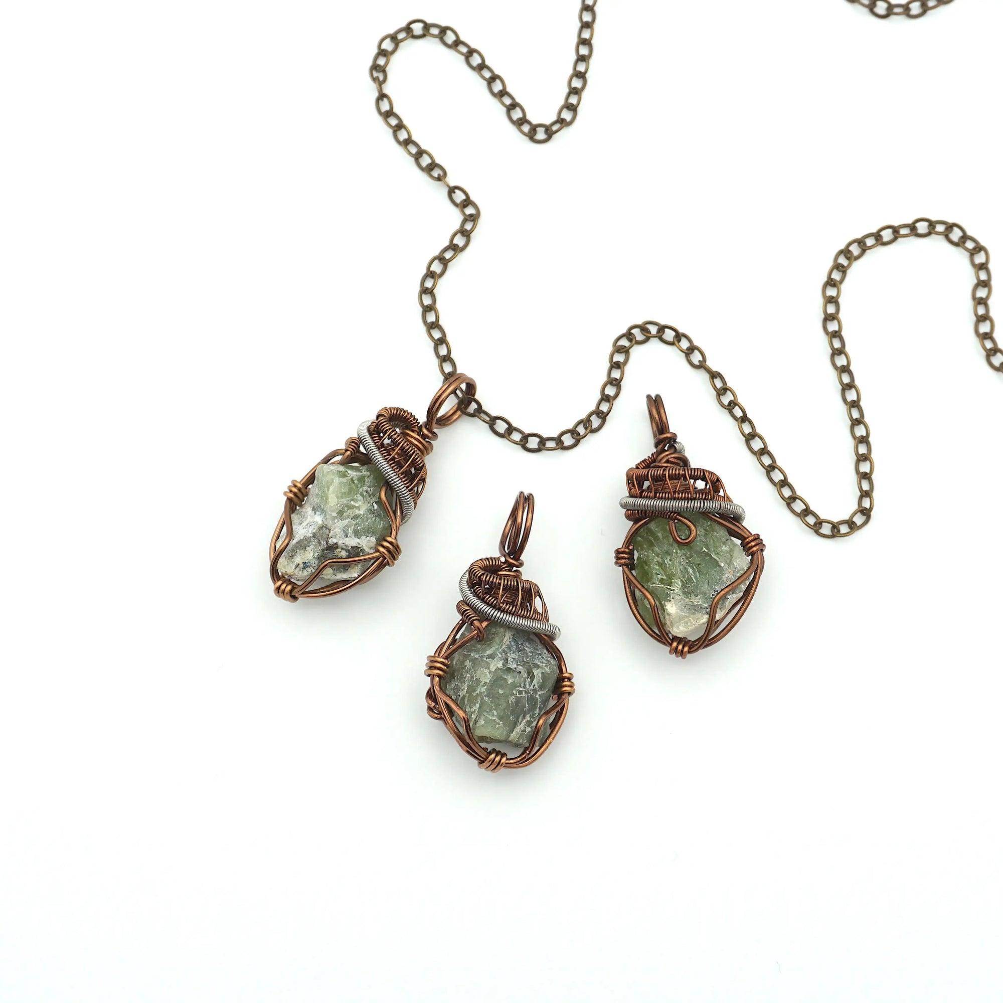 Three raw peridot pendants for men showing natural variation in size, shape, and olive green colour — handcrafted two-tone wire wrapped August birthstone necklaces