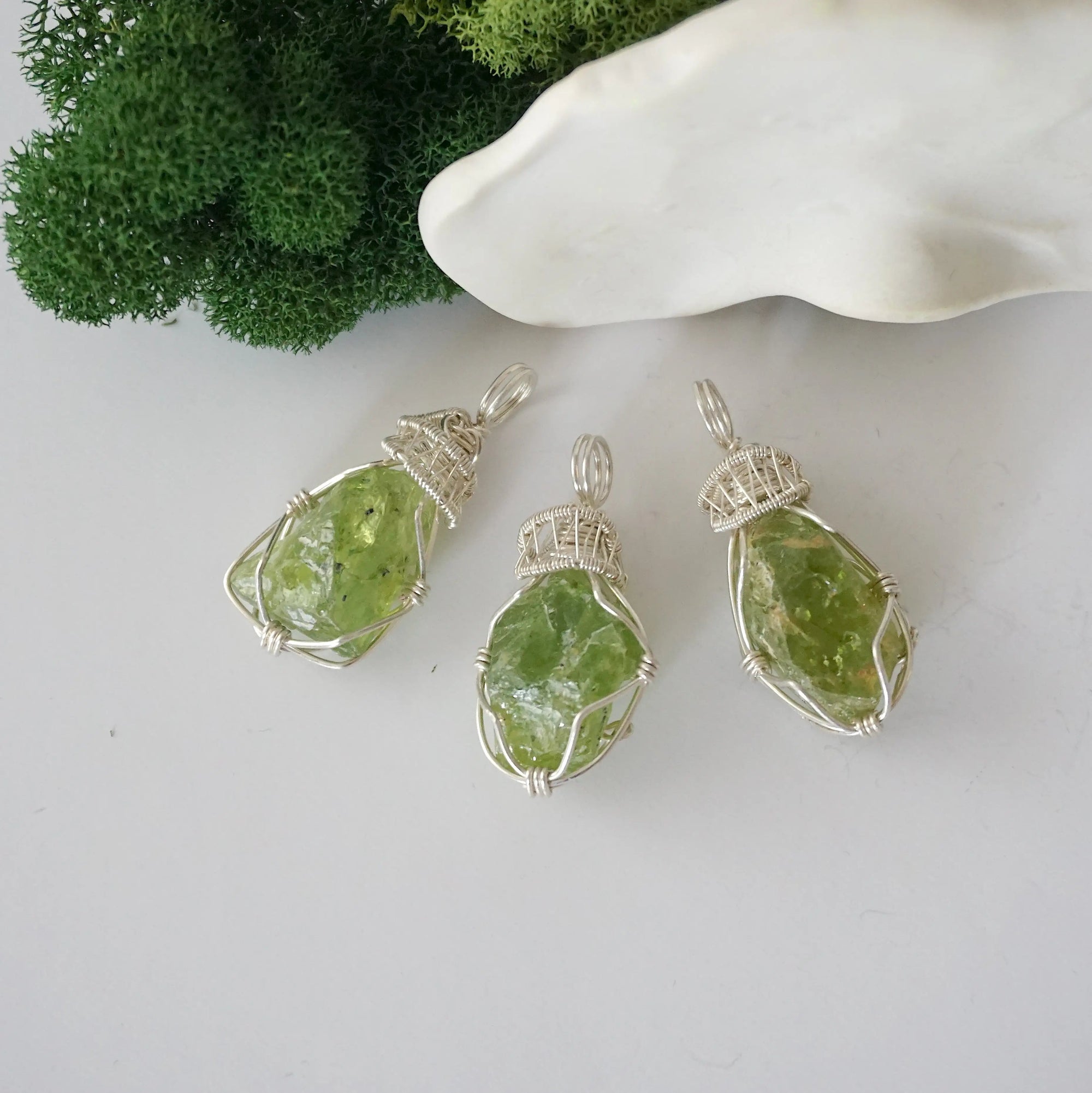 Three raw peridot pendants showing natural variation in stone size, shape, and green colour — each one of a kind, August birthstone, 925 sterling silver wire wrapped, Designs by Nature Gems