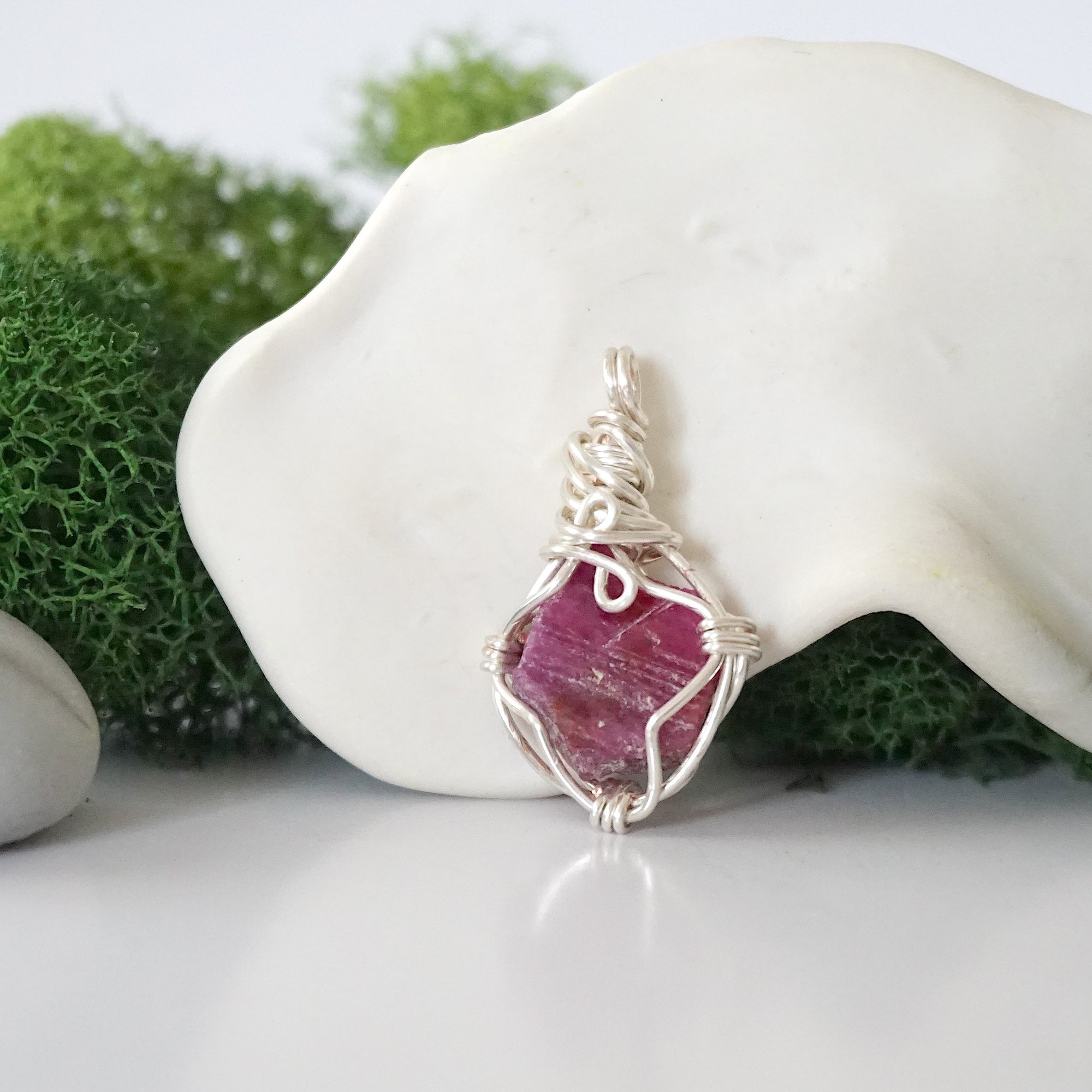 Back angle look at simple raw pink ruby pendant with silver wire wrapping