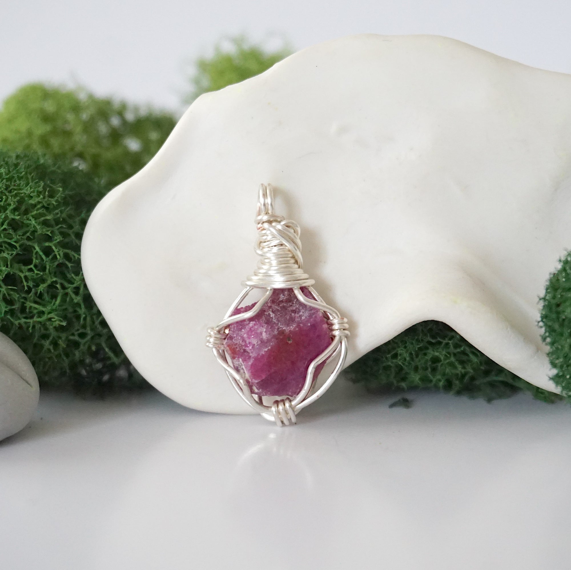 Detailed front angle view of simple raw pink ruby pendant in silver wire