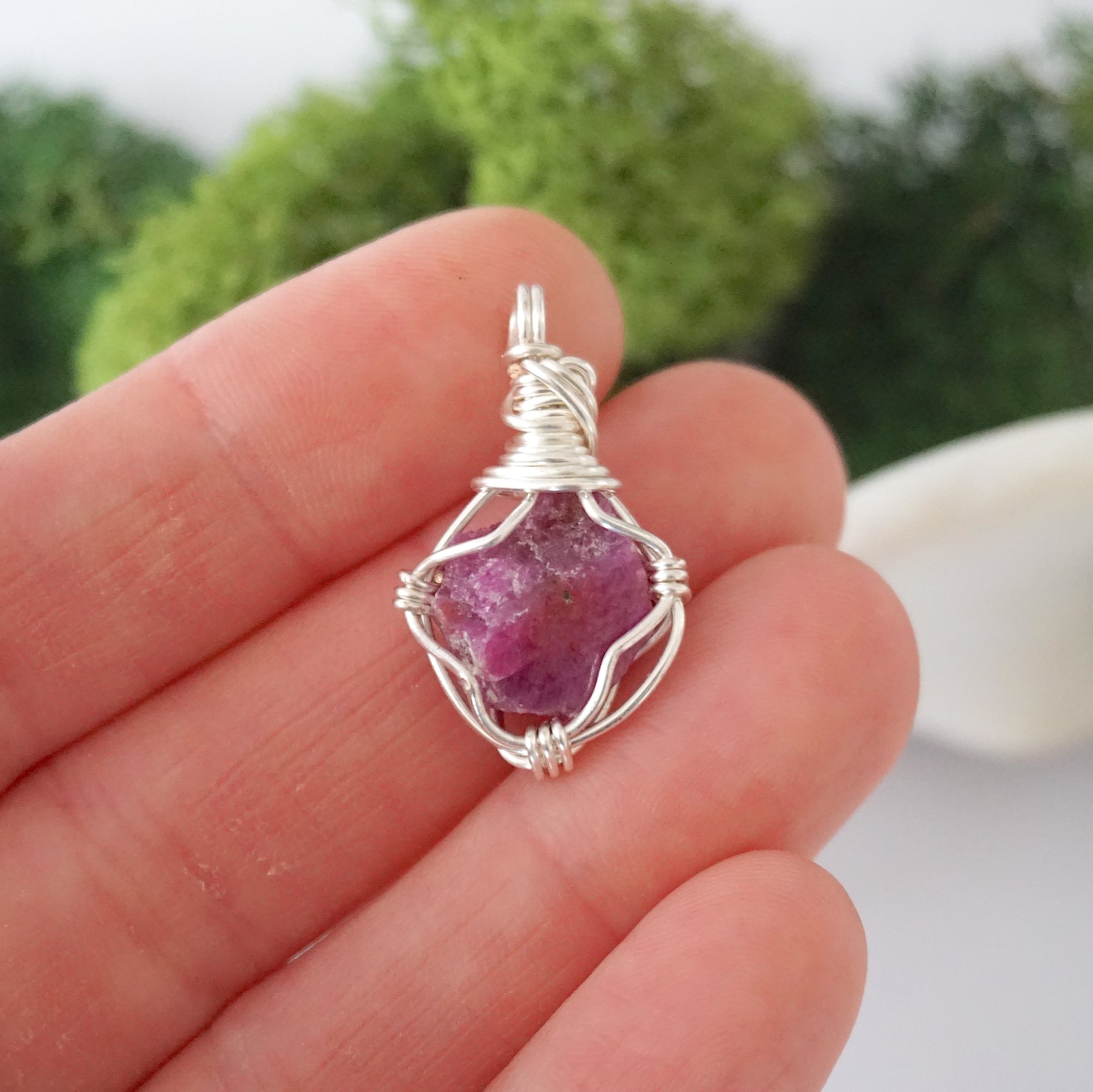 Simple raw pink ruby pendant shown in hand for size reference
