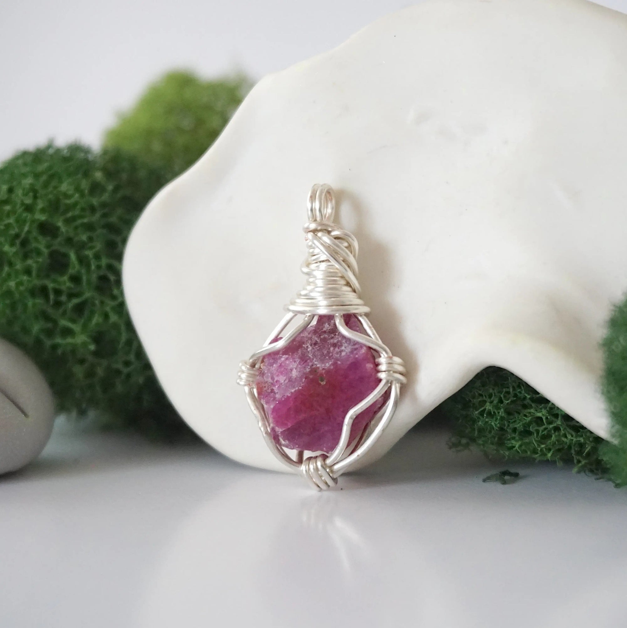 Detailed side angle view of simple raw pink ruby pendant in silver wire