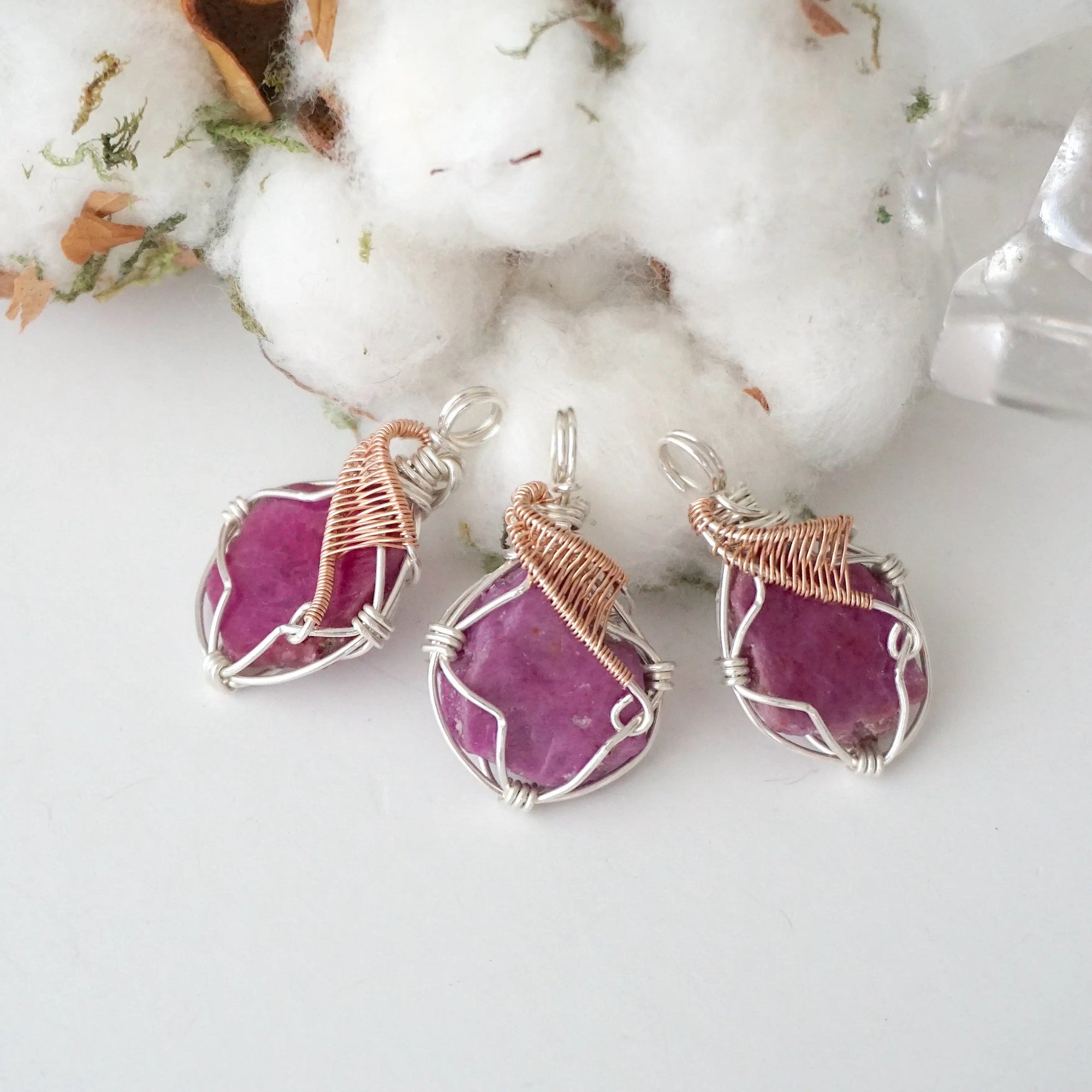 Three raw pink ruby pendants in sterling silver and 14k rose gold filled, showing natural variation in size, shape, and color. Handcrafted July birthstone jewelry by Designs by Nature Gems.