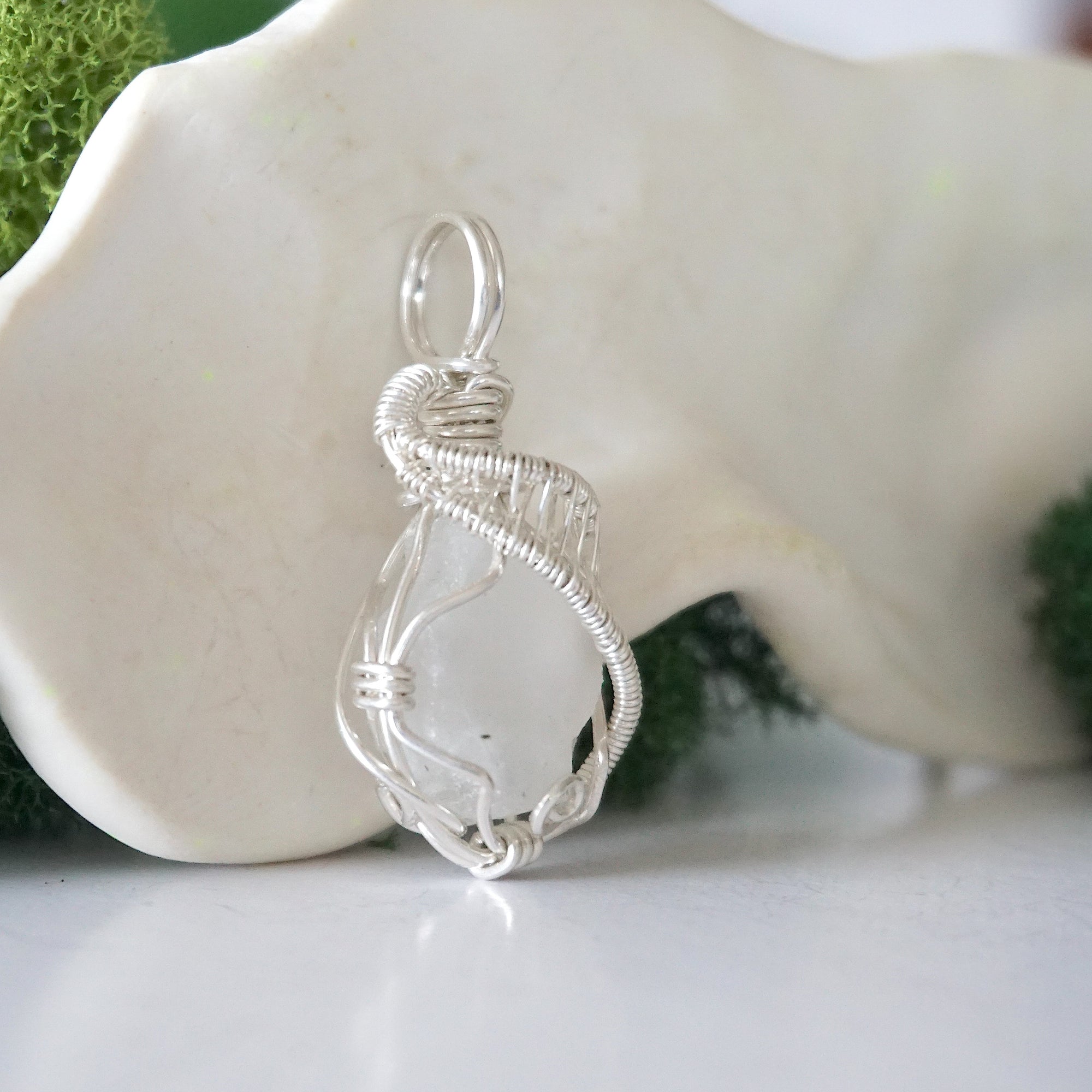 Side angle of raw rainbow moonstone pendant showing artisan wire wrapped sterling silver detail