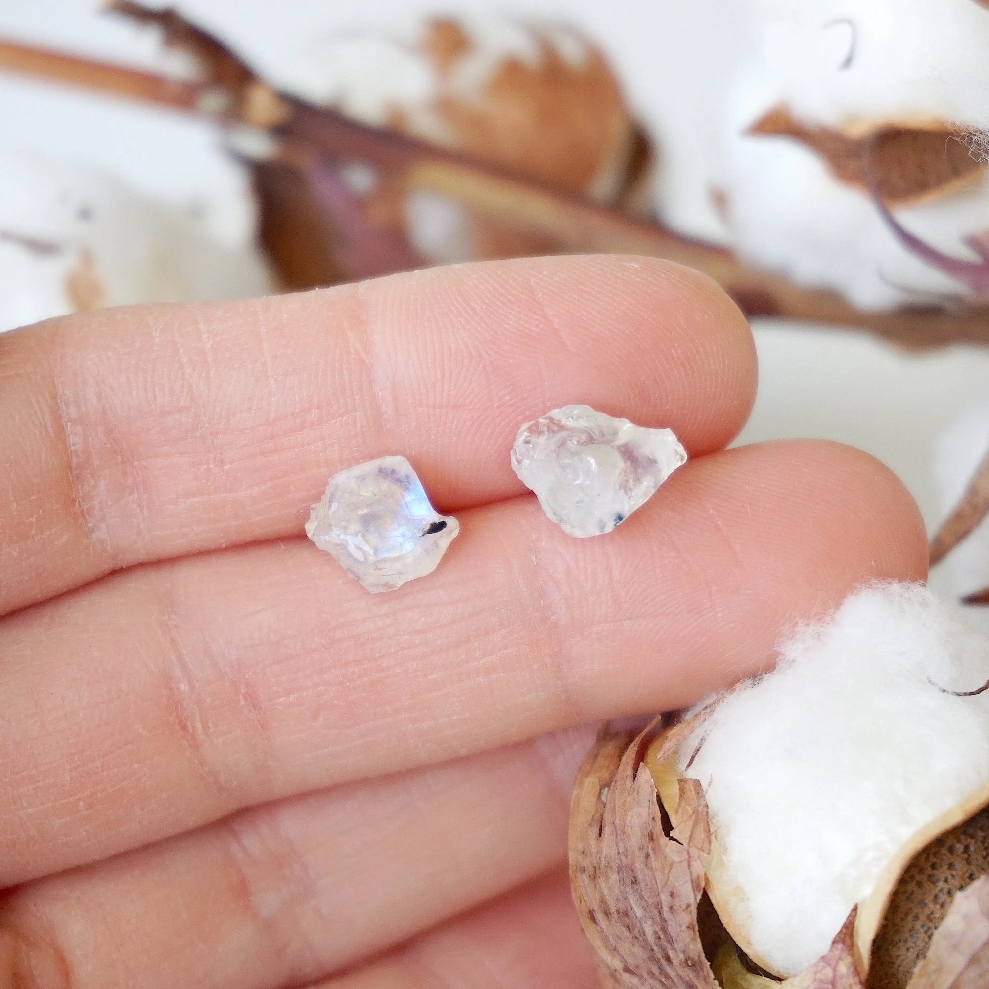 Raw rainbow moonstone stud earrings in hand showing natural 6–9mm moonstone stones on 925 sterling silver posts, June birthstone studs.