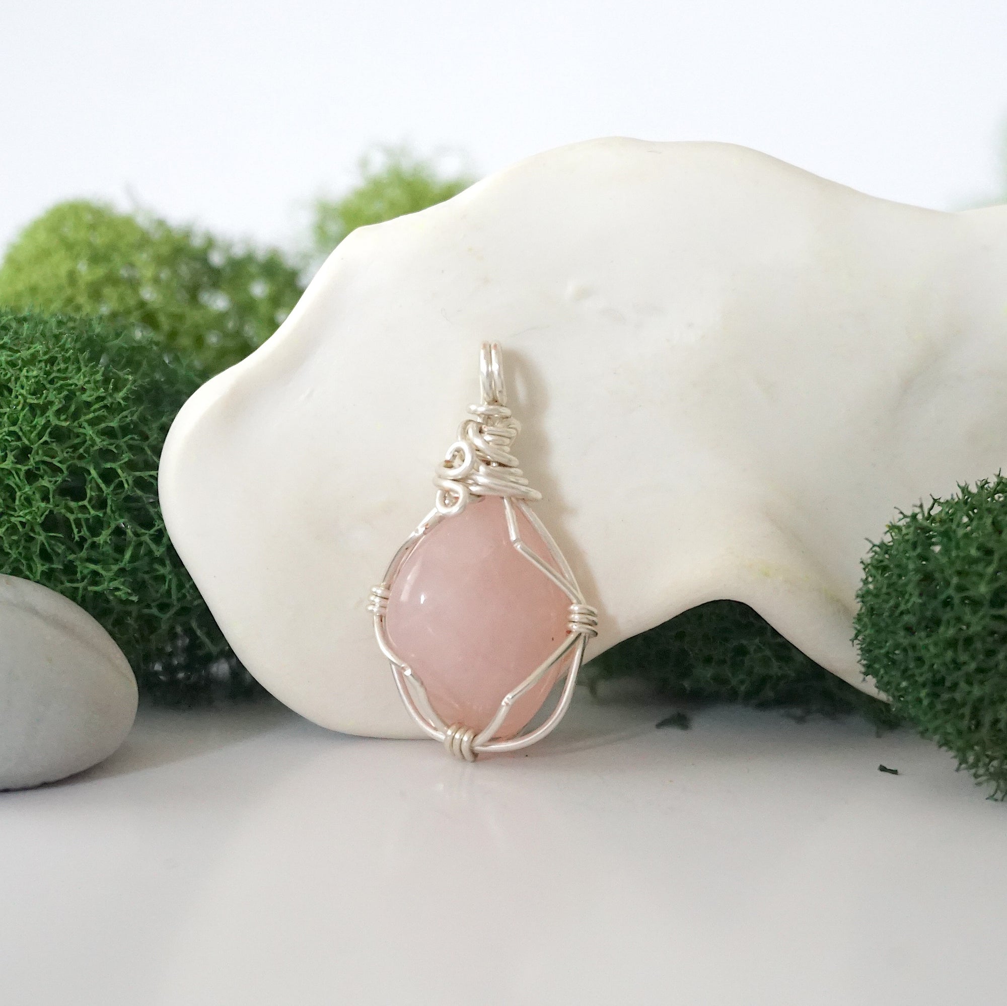 Back angle look at simple raw rose quartz pendant with silver wire wrapping
