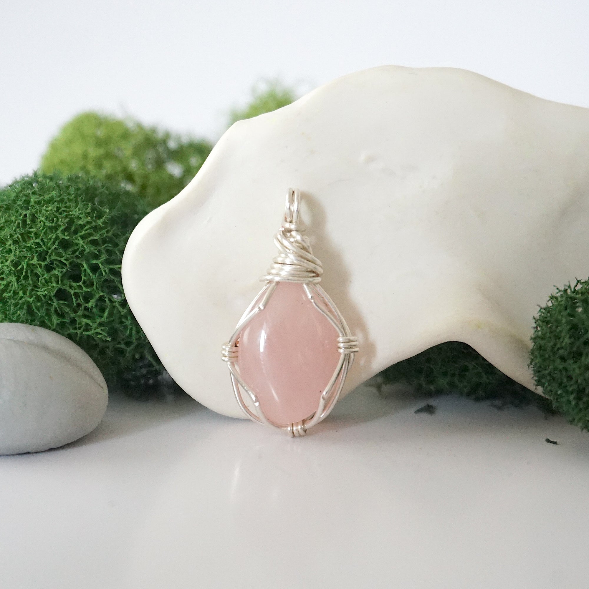 Detailed front angle view of simple raw rose quartz pendant in silver wire