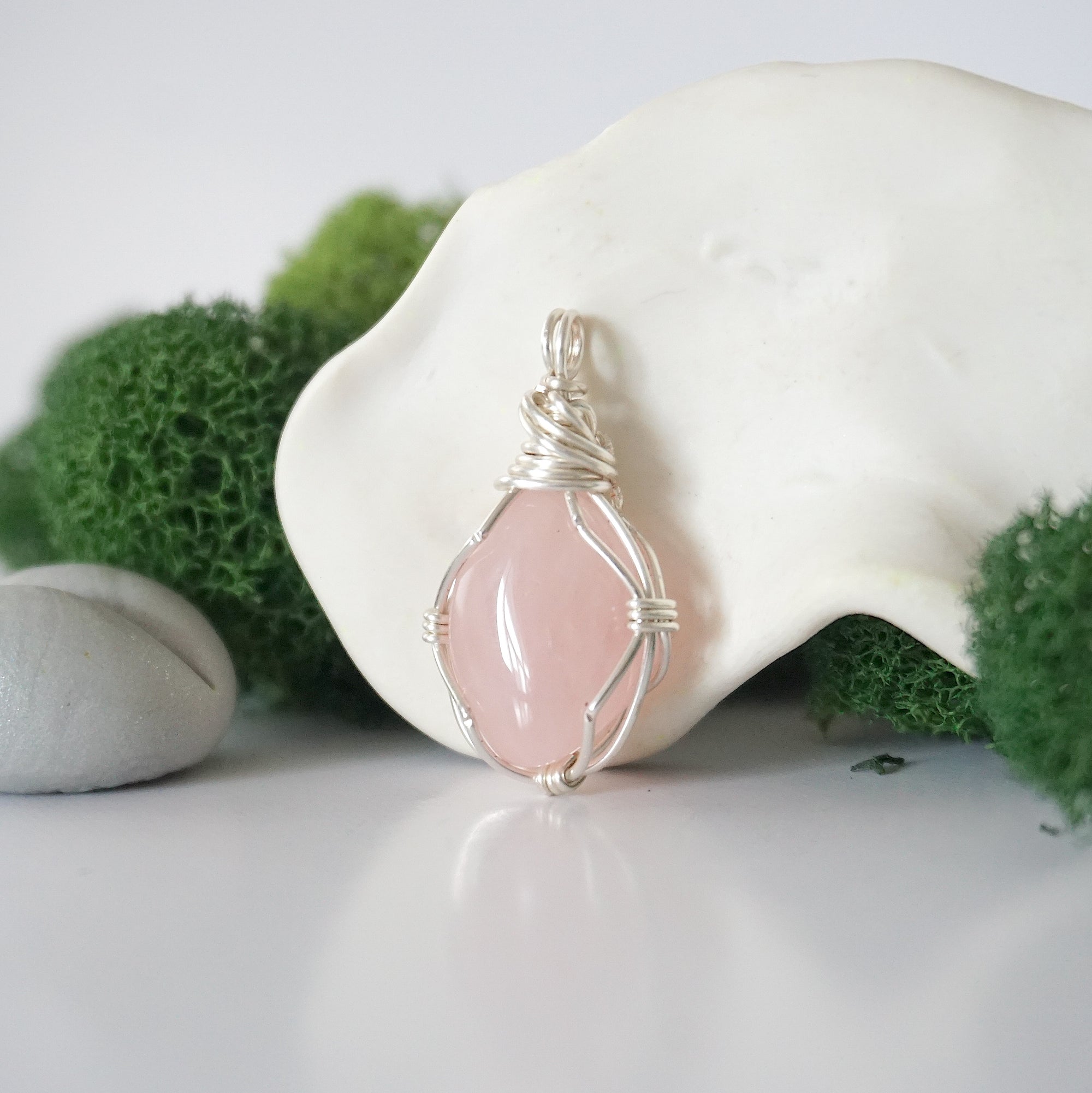 Detailed side angle view of simple raw rose quartz pendant in silver wire