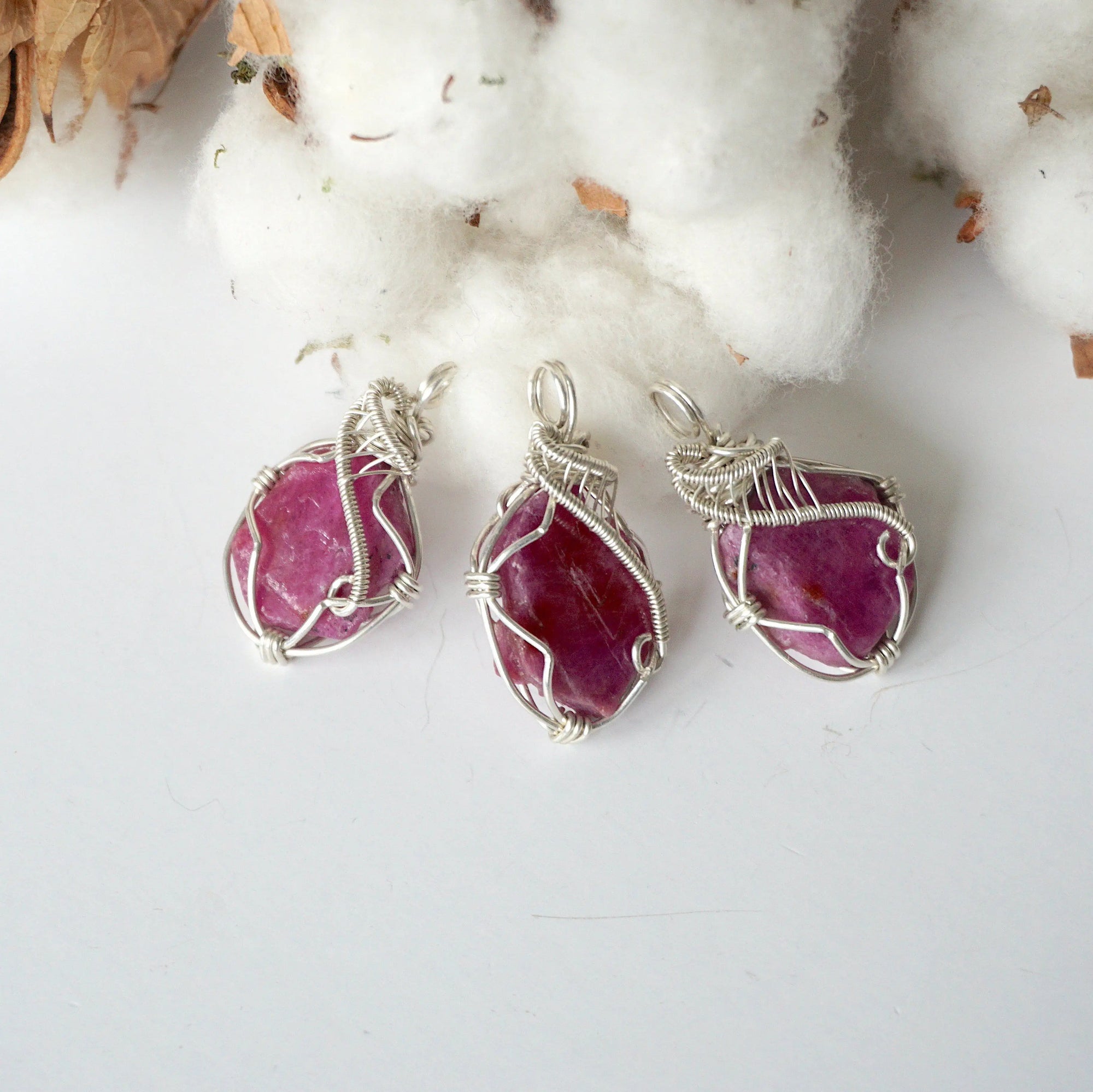 Three raw ruby pendants showing natural variation in color, size, and shape, sterling silver artisan wire wrapped