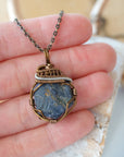 Raw sapphire pendant held in hand to show size — wire wrapped in antique bronze and dark silver, handcrafted crystal necklace by Designs by Nature Gems