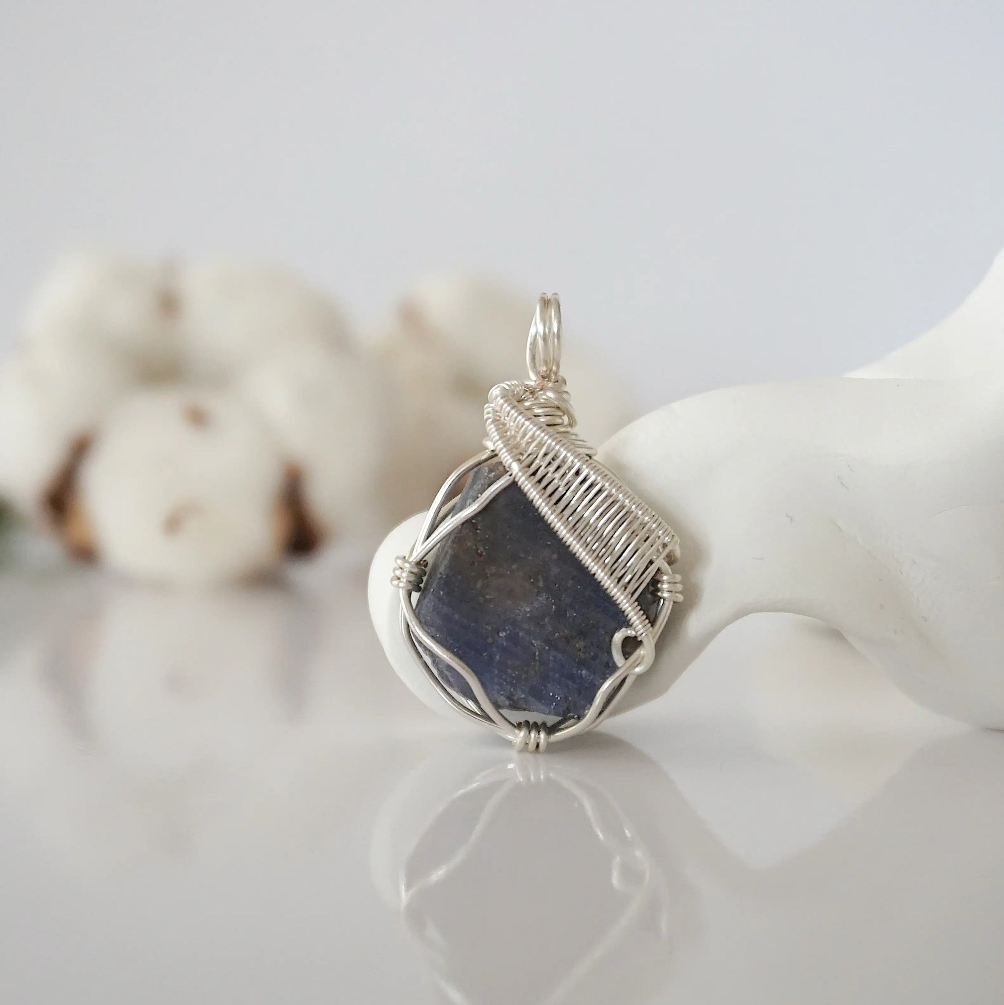 Front view of raw sapphire pendant — natural unpolished dark blue corundum stone hand-wrapped in detailed silver finish wire, handcrafted artisan crystal jewelry