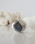 Front view of raw sapphire pendant — natural unpolished dark blue corundum stone hand-wrapped in detailed silver finish wire, handcrafted artisan crystal jewelry