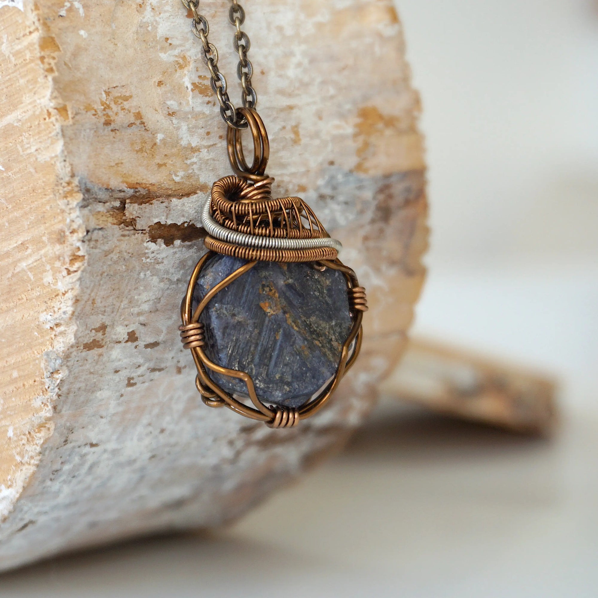 Right-angle detail of raw sapphire pendant showing artisan wire-wrapping in antique bronze and dark silver — handcrafted crystal necklace