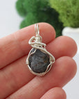 Handmade raw sapphire pendant held in hand showing size — natural dark blue sapphire stone wire wrapped in 925 sterling silver, 25-30 carats, one of a kind