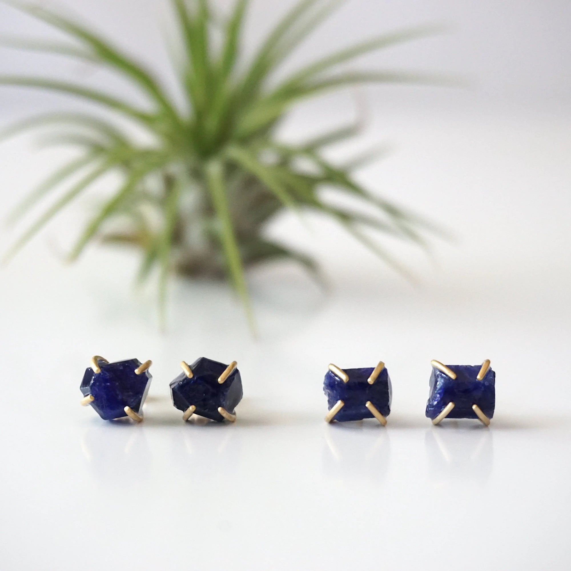 Two pairs of raw sapphire stud earrings showing natural variation in stone shape, size, and shade of blue — each pair is one of a kind