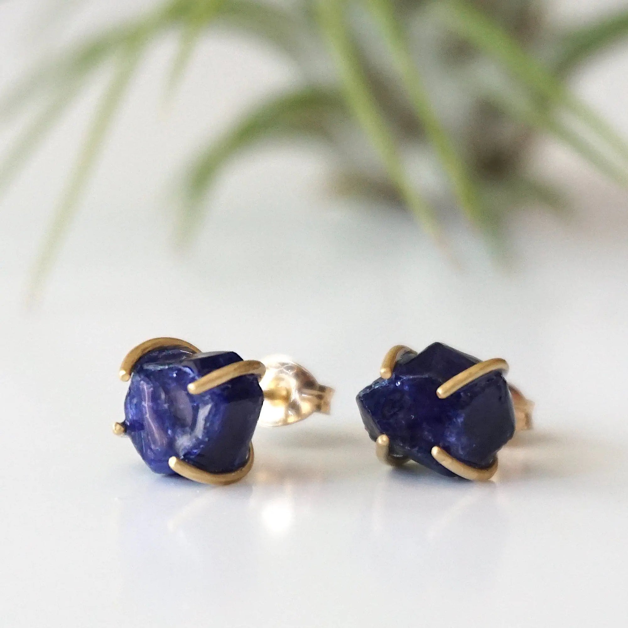 Slight-angle view of genuine raw sapphire stud earrings in 14k gold vermeil prong settings — minimalist September birthstone jewelry