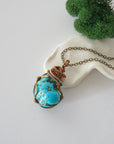 Raw turquoise necklace with detailed antique bronze copper wire wrapping on chain, handmade crystal pendant flat lay