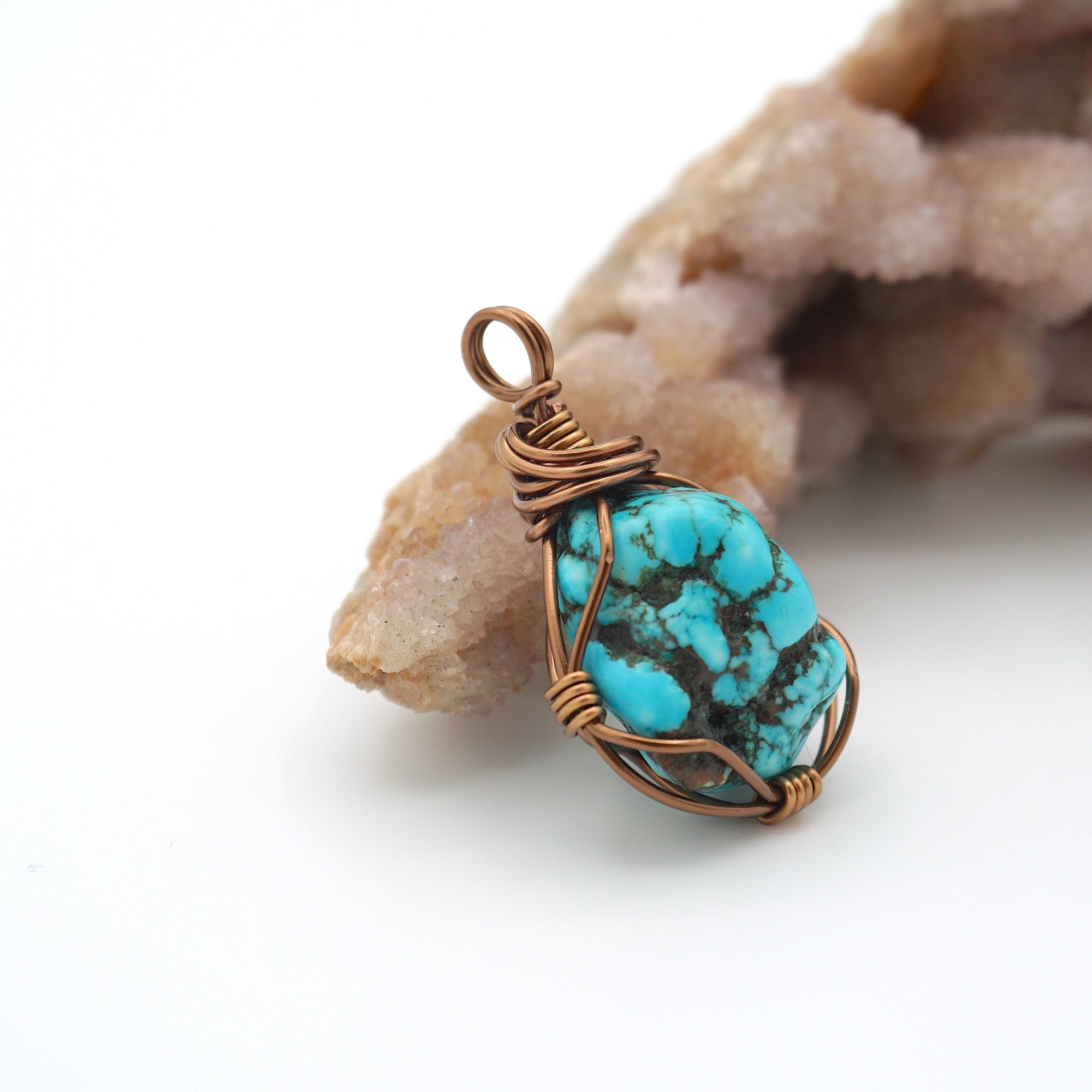 Side angle of handmade raw turquoise pendant showing copper wire wrapping detail and natural unpolished crystal texture