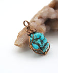 Side angle of handmade raw turquoise pendant showing copper wire wrapping detail and natural unpolished crystal texture
