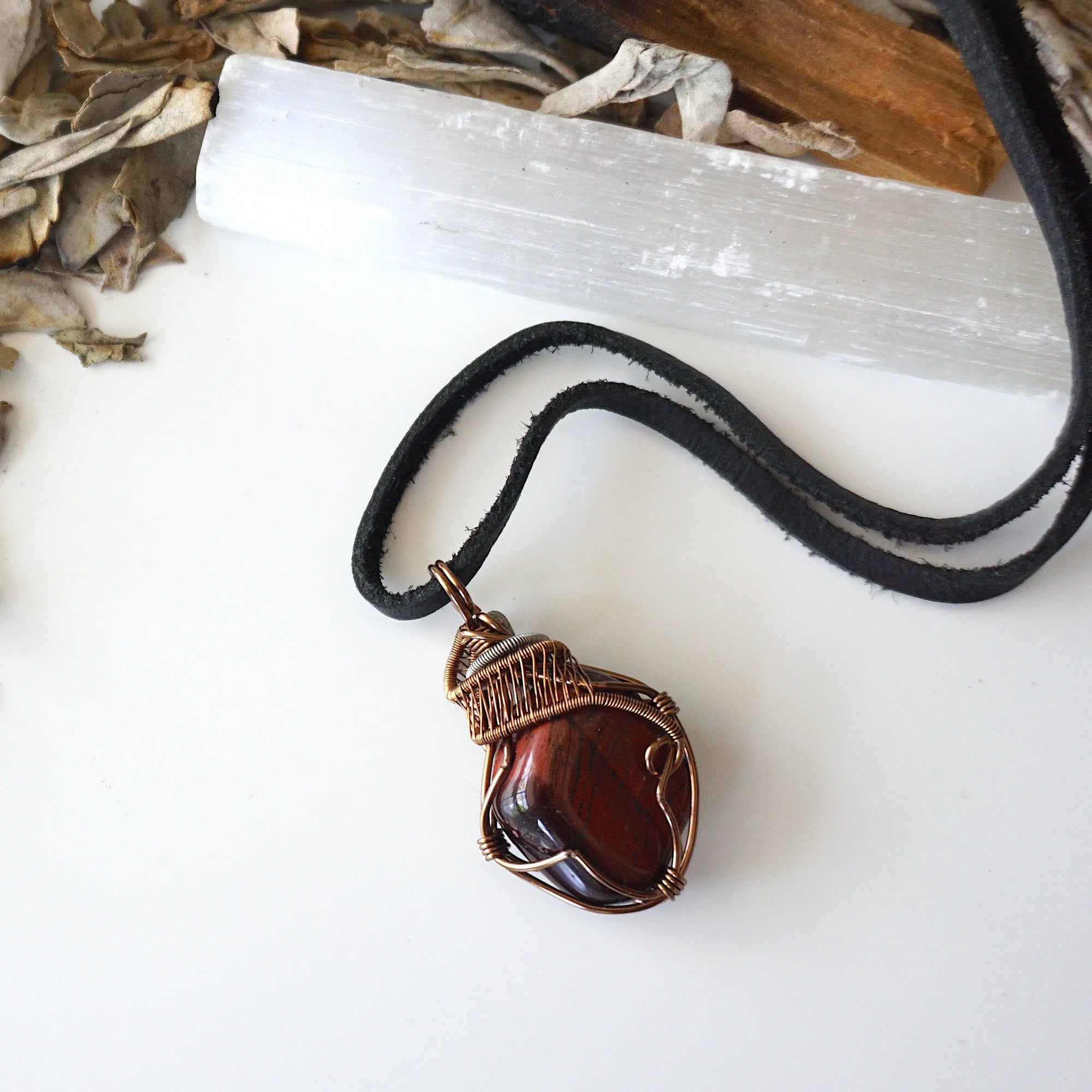Natural red tiger's eye pendant on black leather cord, laying flat, handcrafted by Designs by Nature Gems.