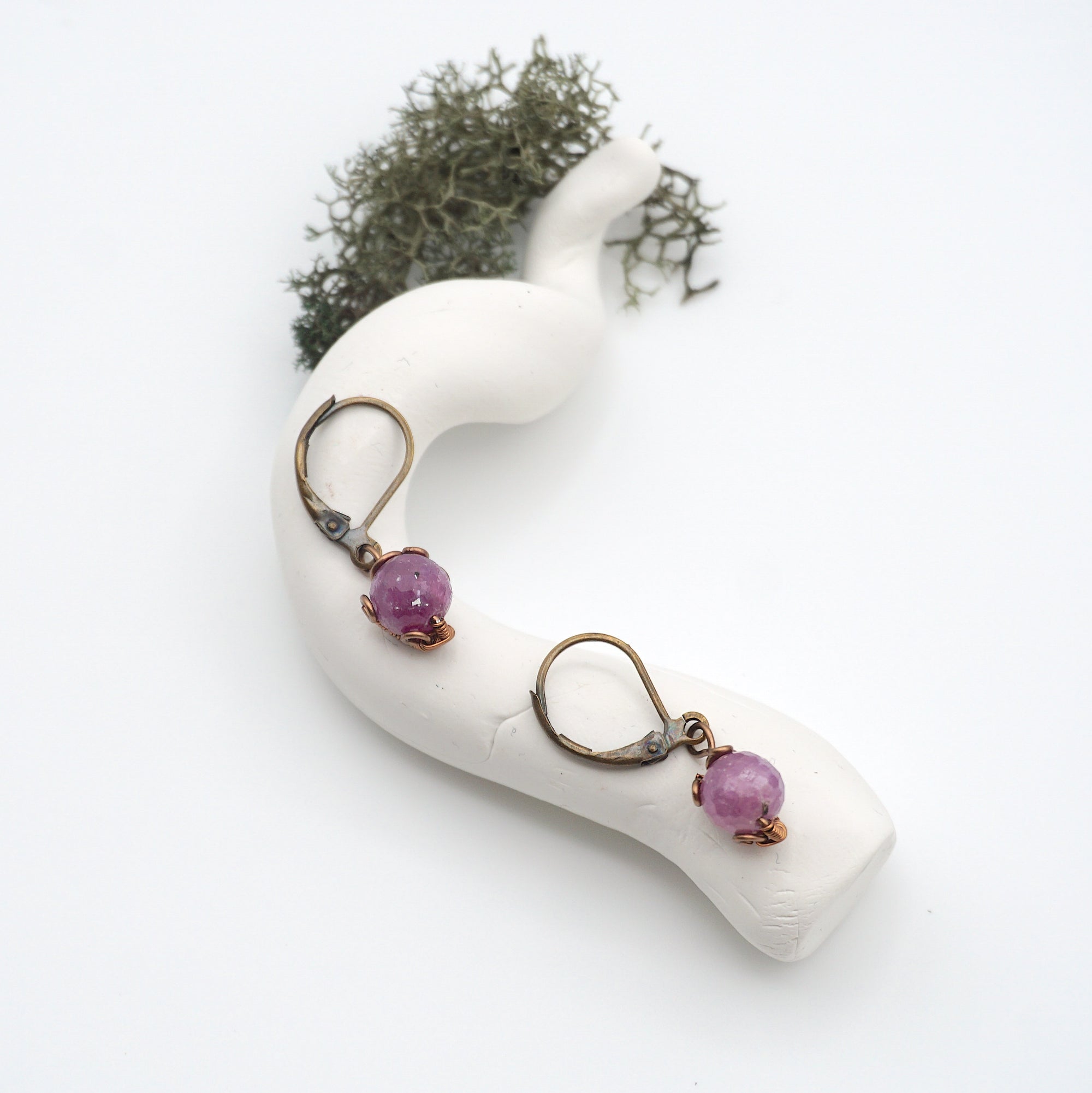 Bird’s eye view of ruby drop earrings laying flat on a display, showing detailed wire wrapping and gemstone color.