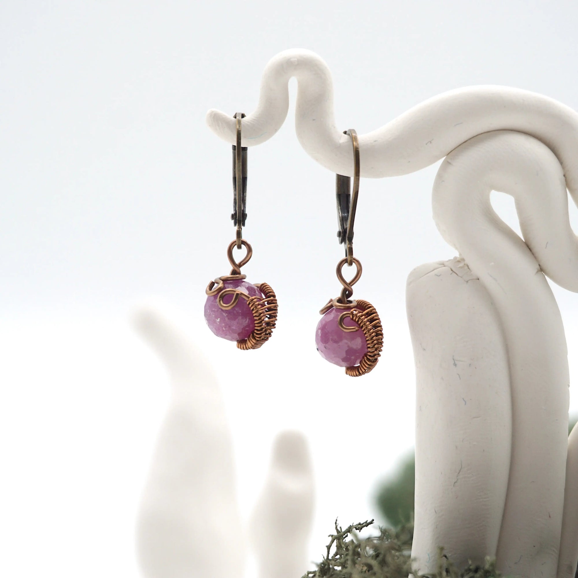 Close-up of handcrafted ruby drop earrings with antique bronze copper wire wrapping.
