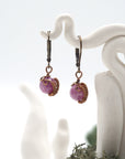 Close-up of handcrafted ruby drop earrings with antique bronze copper wire wrapping.