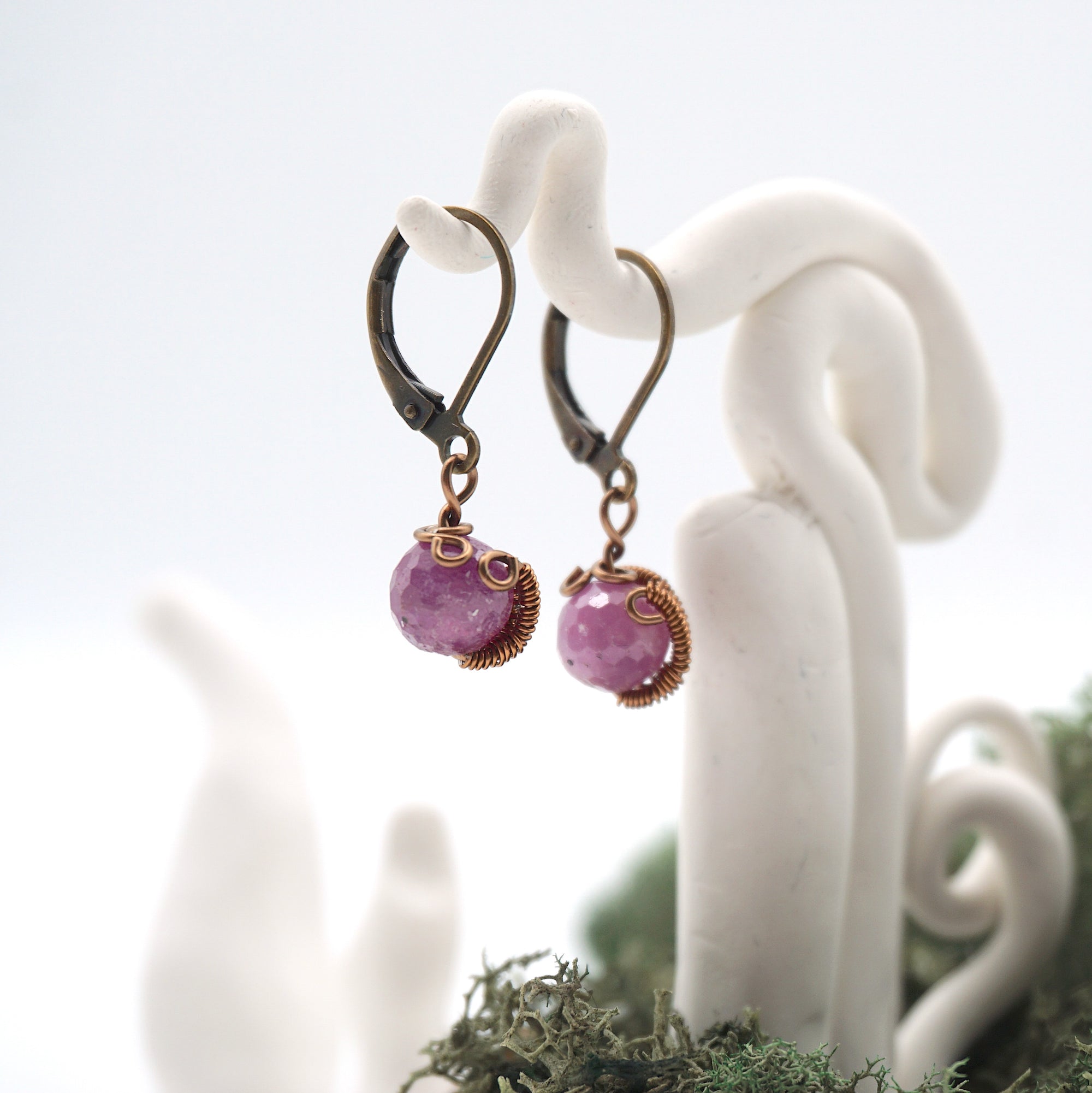 Side angle of ruby drop earrings on a display stand, highlighting antique bronze copper wire wrapping.