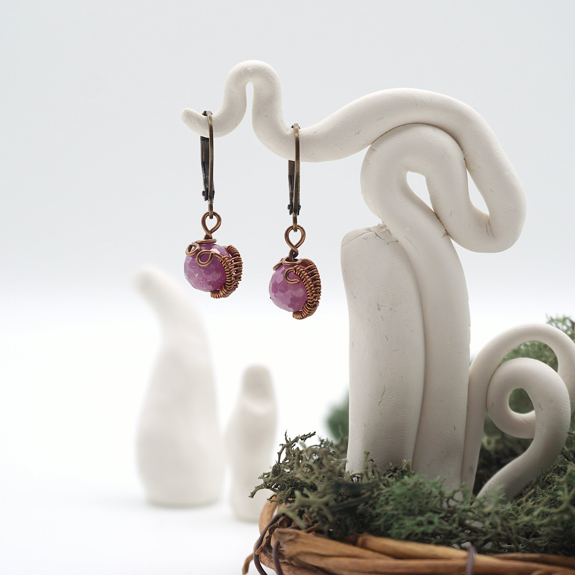 Front angle of ruby drop earrings hanging on a jewelry display, wire-wrapped design.