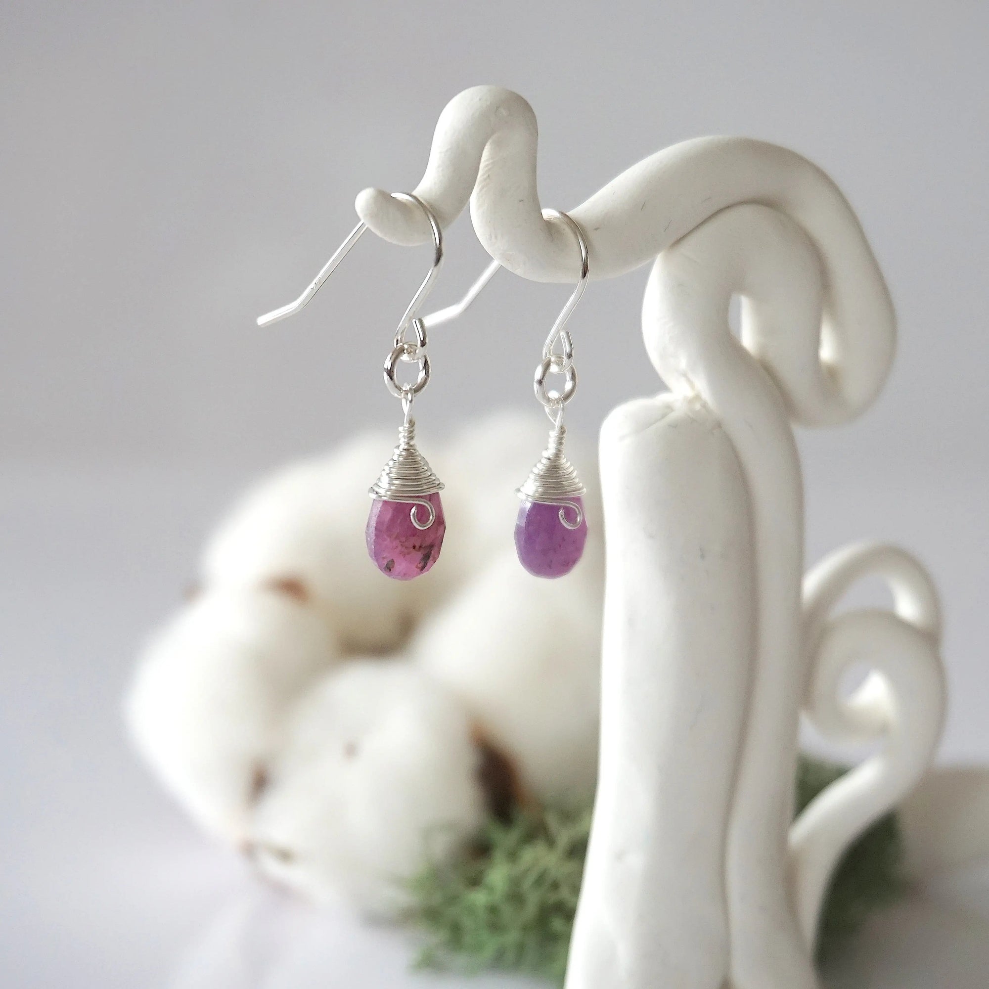 Side view of ruby sterling silver drop earrings showing wire wrapped natural faceted ruby, artisan craftsmanship, on a display – Designs by Nature Gems