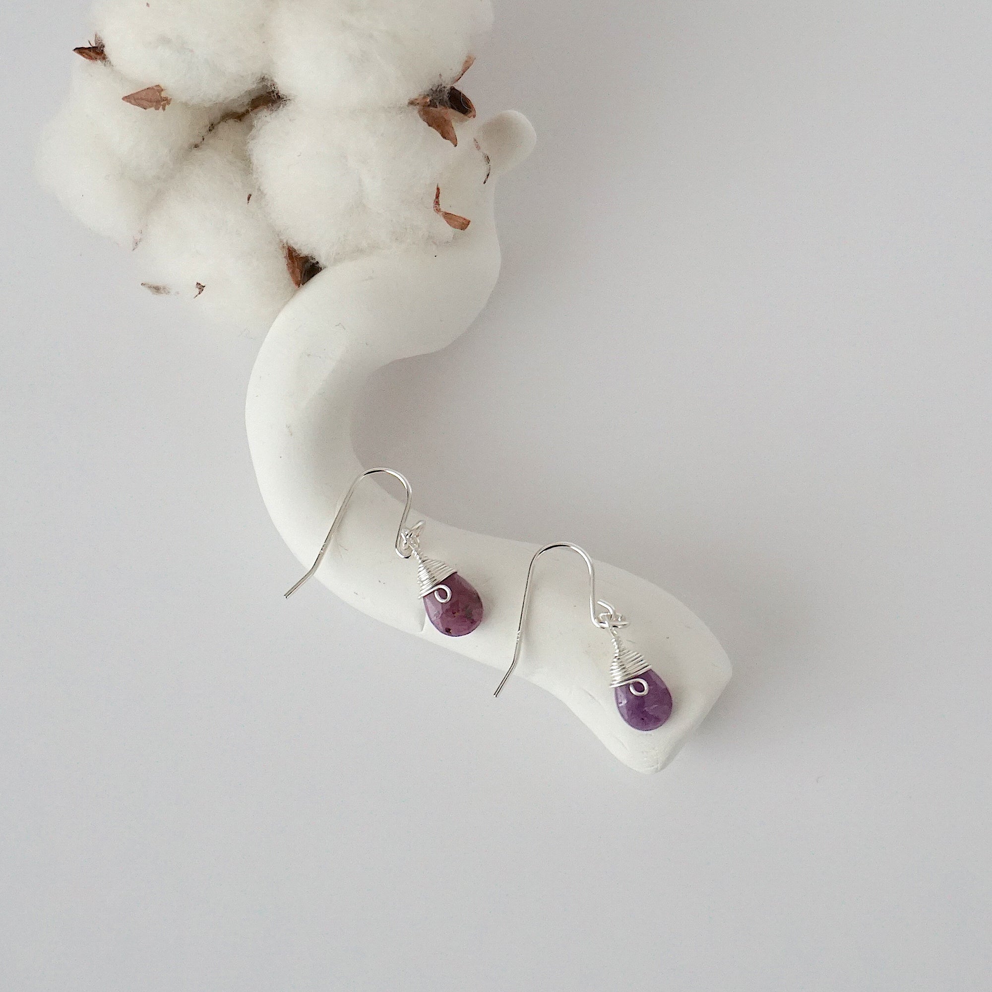 Ruby sterling silver drop earrings with faceted natural ruby stones and wire wrapping, laying flat on a display – Designs by Nature Gems