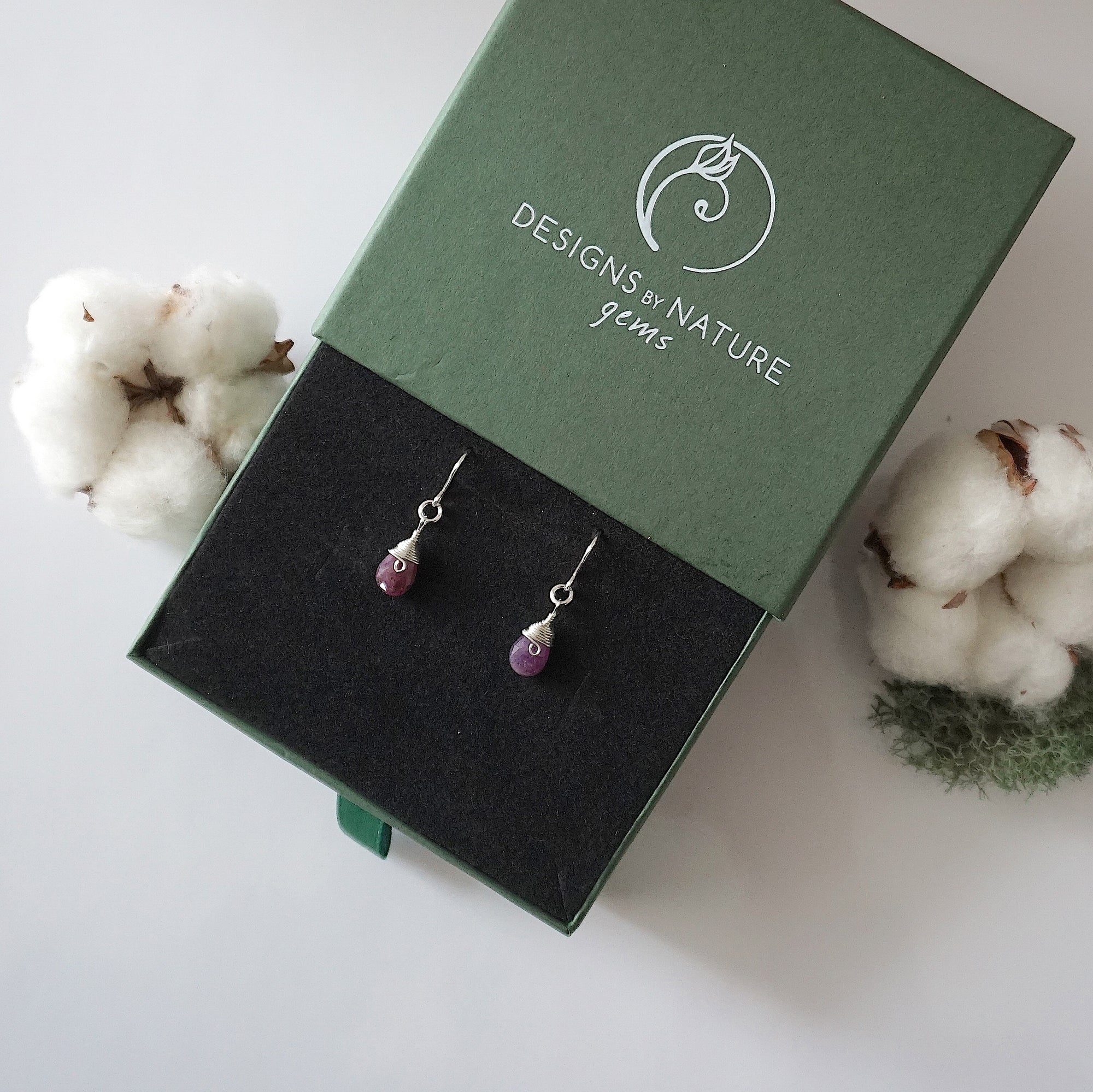 Ruby sterling silver drop earrings in branded Designs by Nature Gems jewelry box, showcasing handcrafted faceted ruby and sterling silver wire wrapping