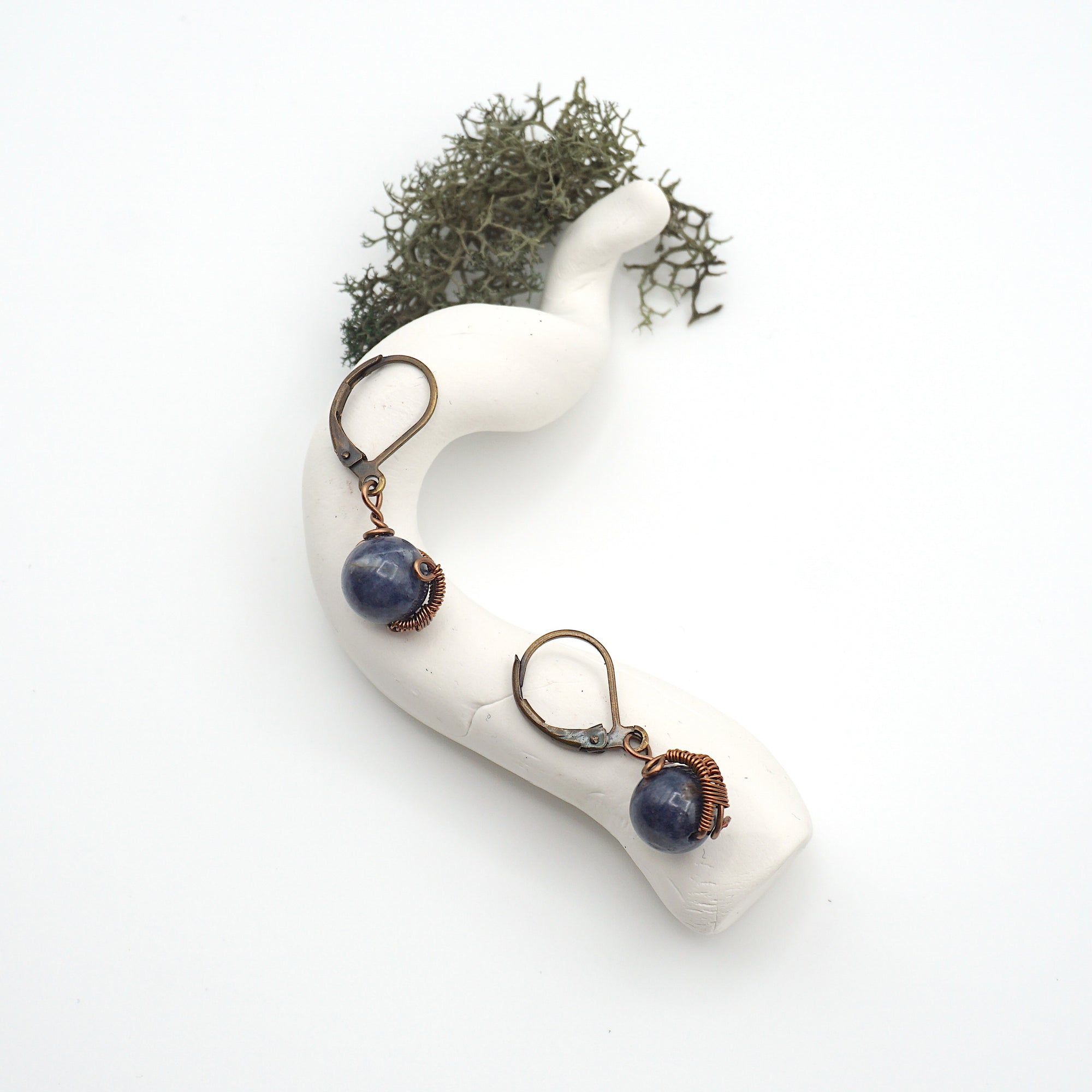 Bird’s eye view of sapphire drop earrings laying flat on a display, showing detailed wire wrapping and gemstone color.