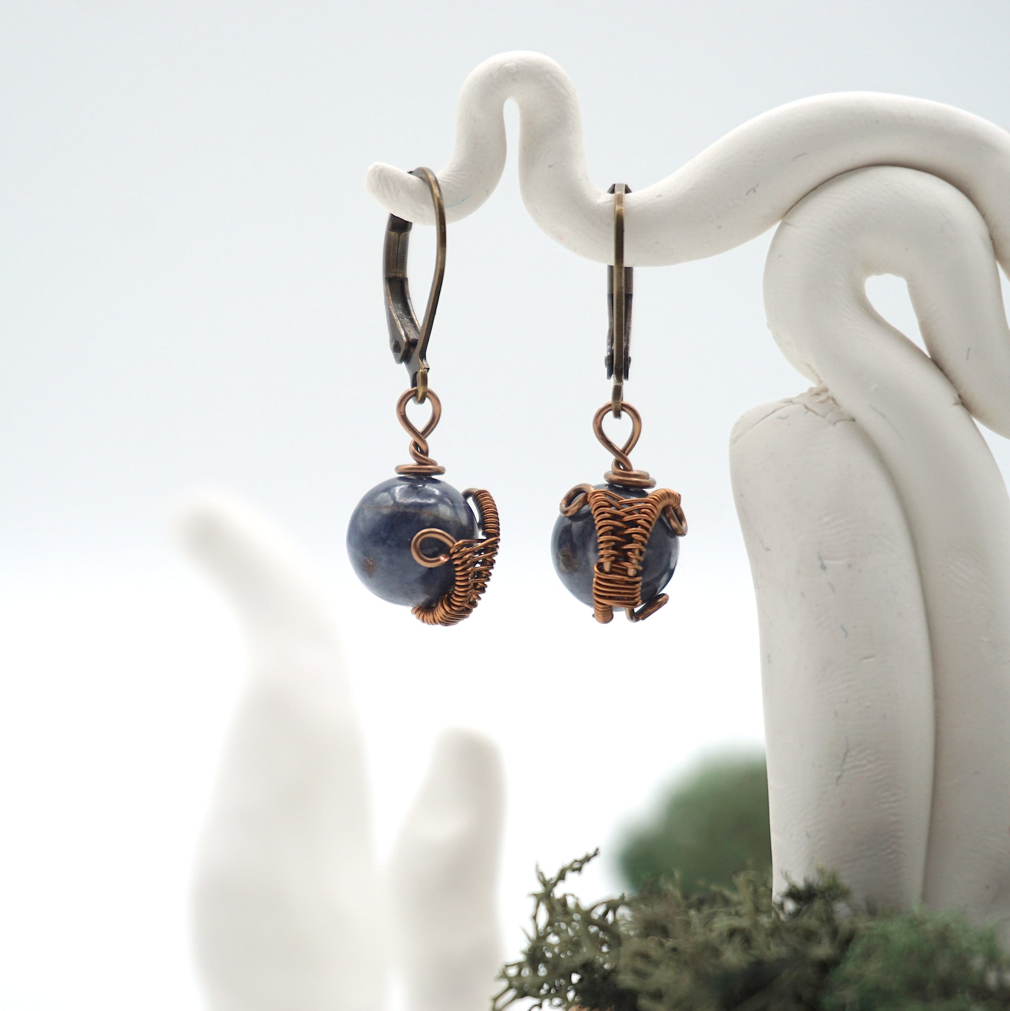 Close-up of handcrafted sapphire drop earrings with antique bronze copper wire wrapping.