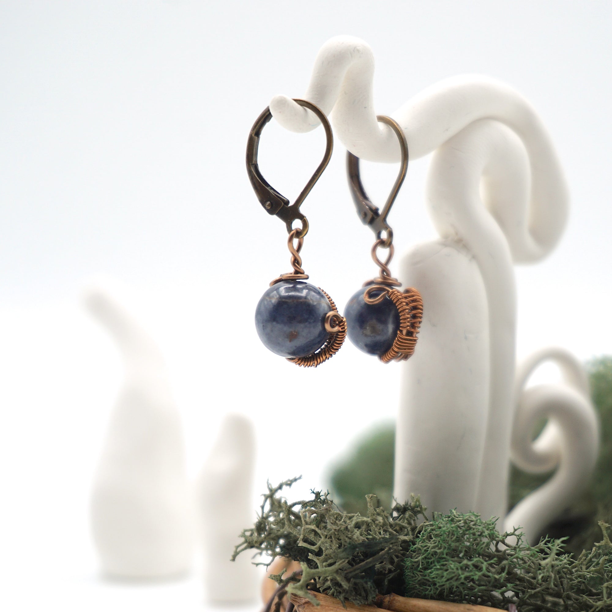 Side angle of sapphire drop earrings on a display stand, highlighting antique bronze copper wire wrapping.


