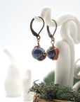 Side angle of sapphire drop earrings on a display stand, highlighting antique bronze copper wire wrapping.


