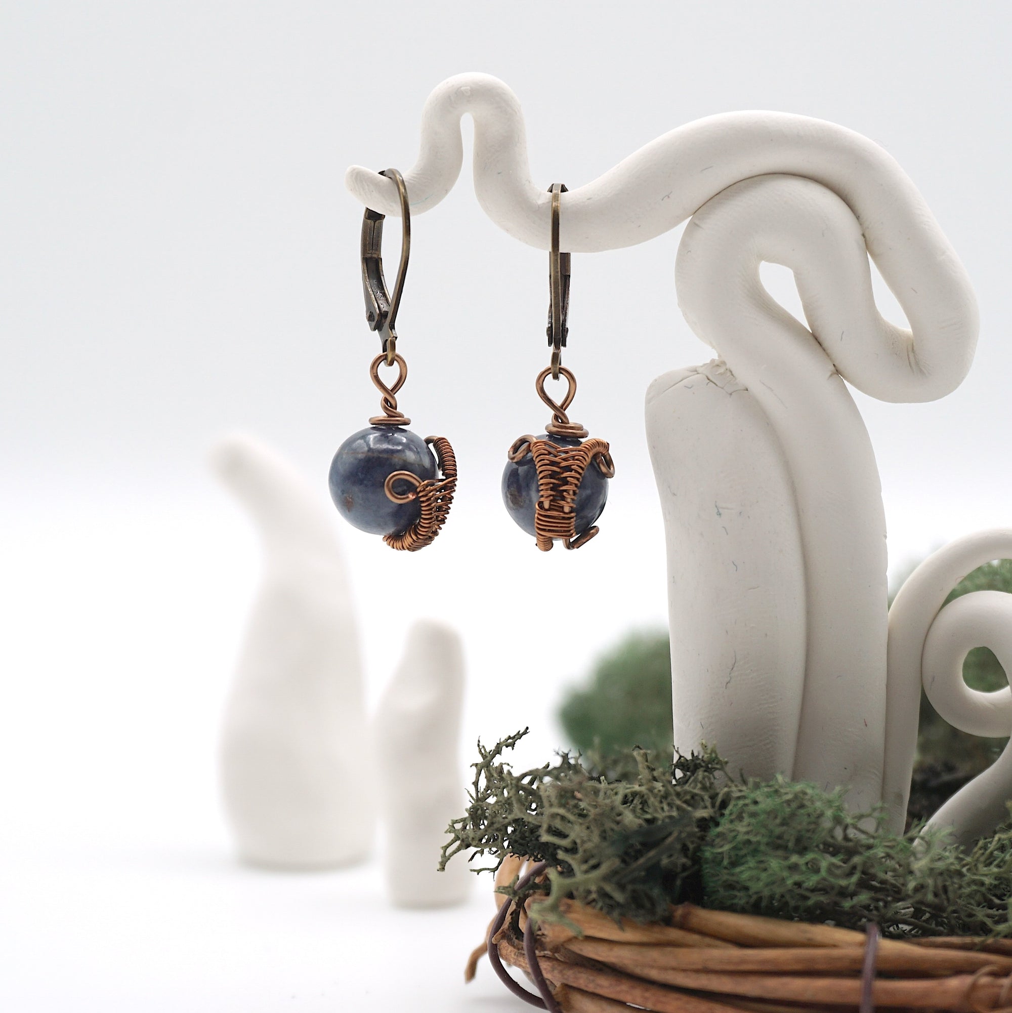 Front angle of sapphire drop earrings hanging on a jewelry display, wire-wrapped design.