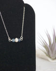 Focused left-side close-up of sterling silver sapphire and pearl bar necklace on jewelry display