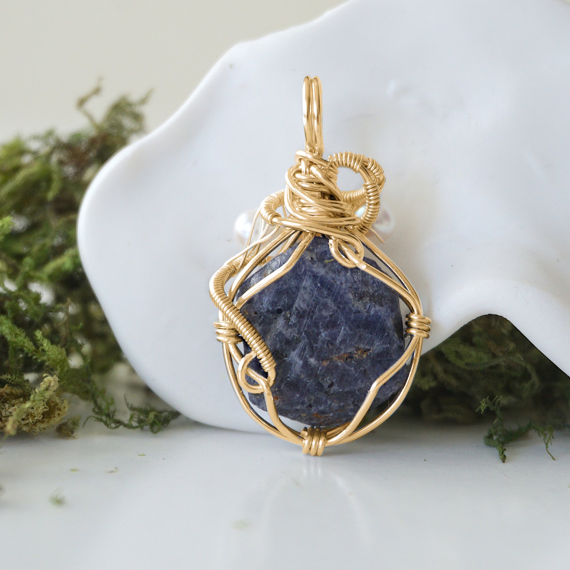 Back angle detail of sapphire and freshwater pearl pendant, showing wire wrapping and natural stone