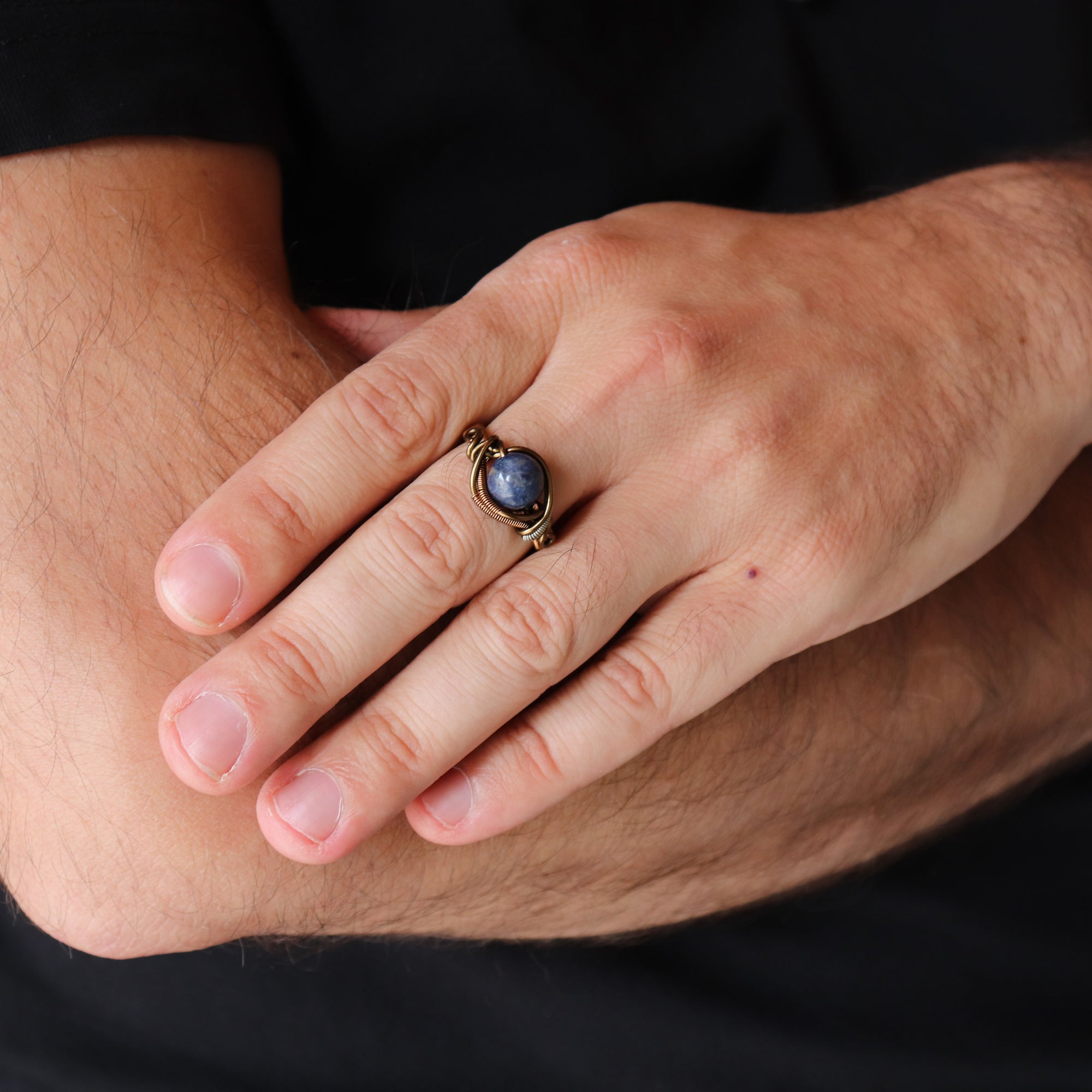Man wearing a natural sapphire ring with antique bronze and dark silver wire wrap — handcrafted all-genders birthstone jewelry