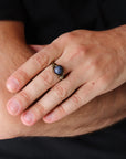 Man wearing a natural sapphire ring with antique bronze and dark silver wire wrap — handcrafted all-genders birthstone jewelry