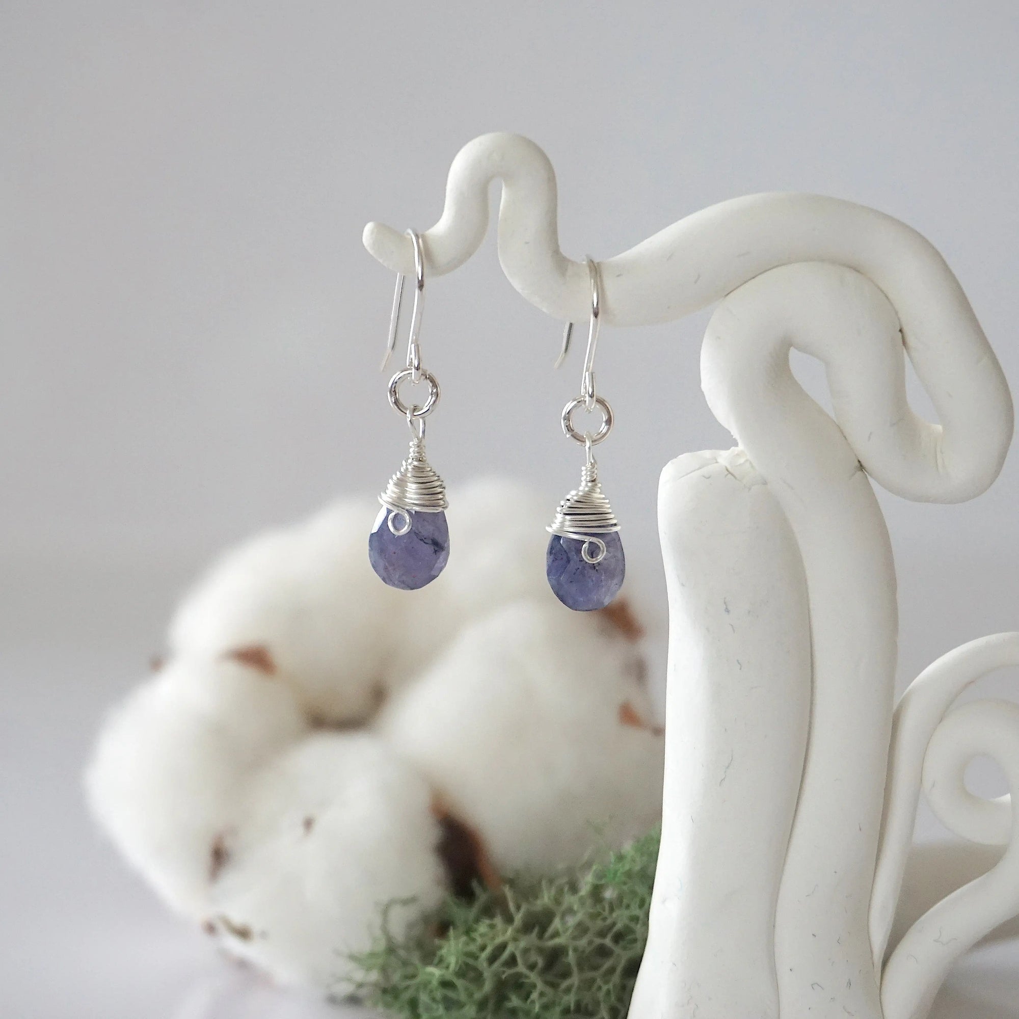 Detailed front view of handcrafted sapphire sterling silver drop earrings with natural faceted sapphire, artisan wire wrapping, hanging from a display – Designs by Nature Gems