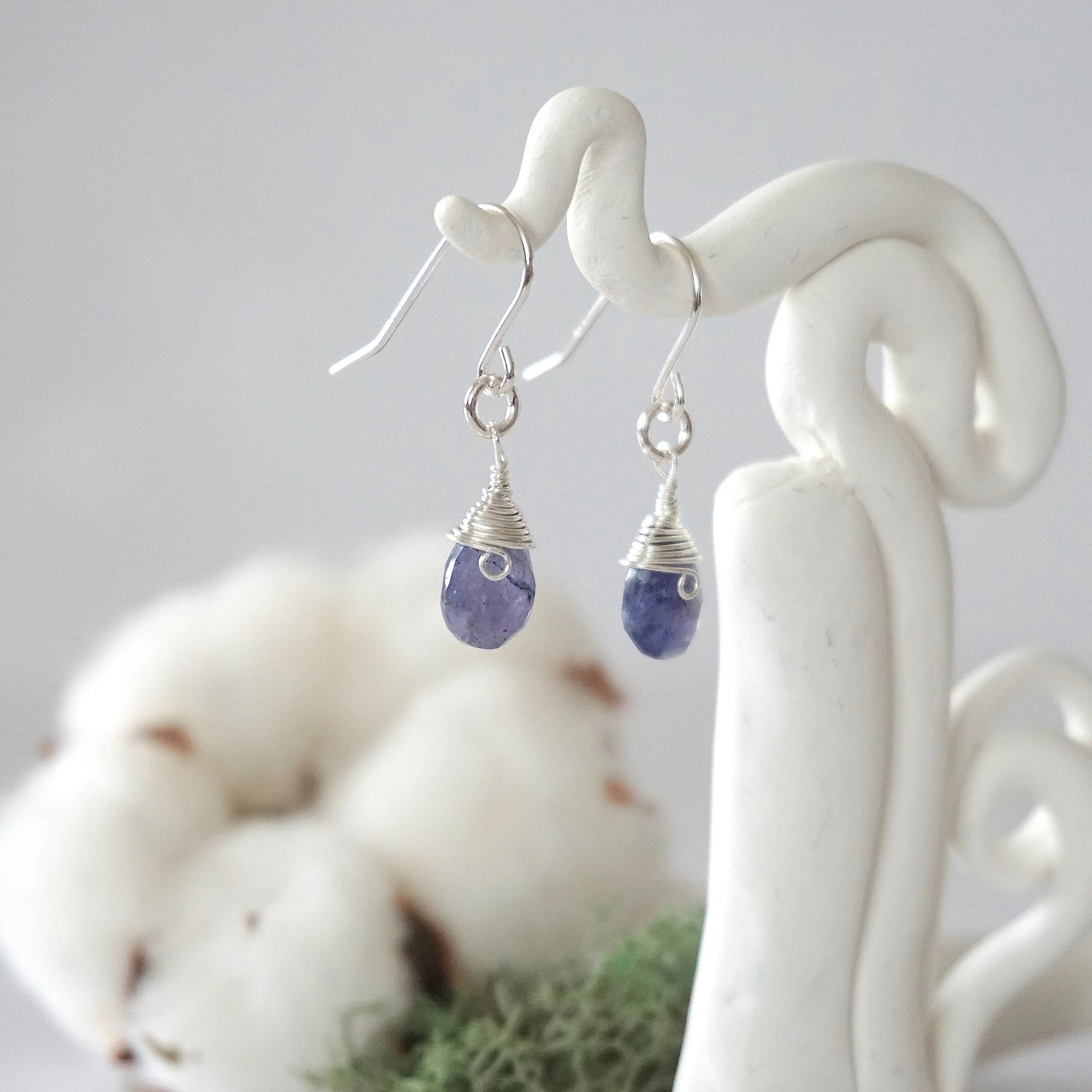 Side view of sapphire sterling silver drop earrings showing wire wrapped natural faceted sapphire, artisan craftsmanship, on a display – Designs by Nature Gems