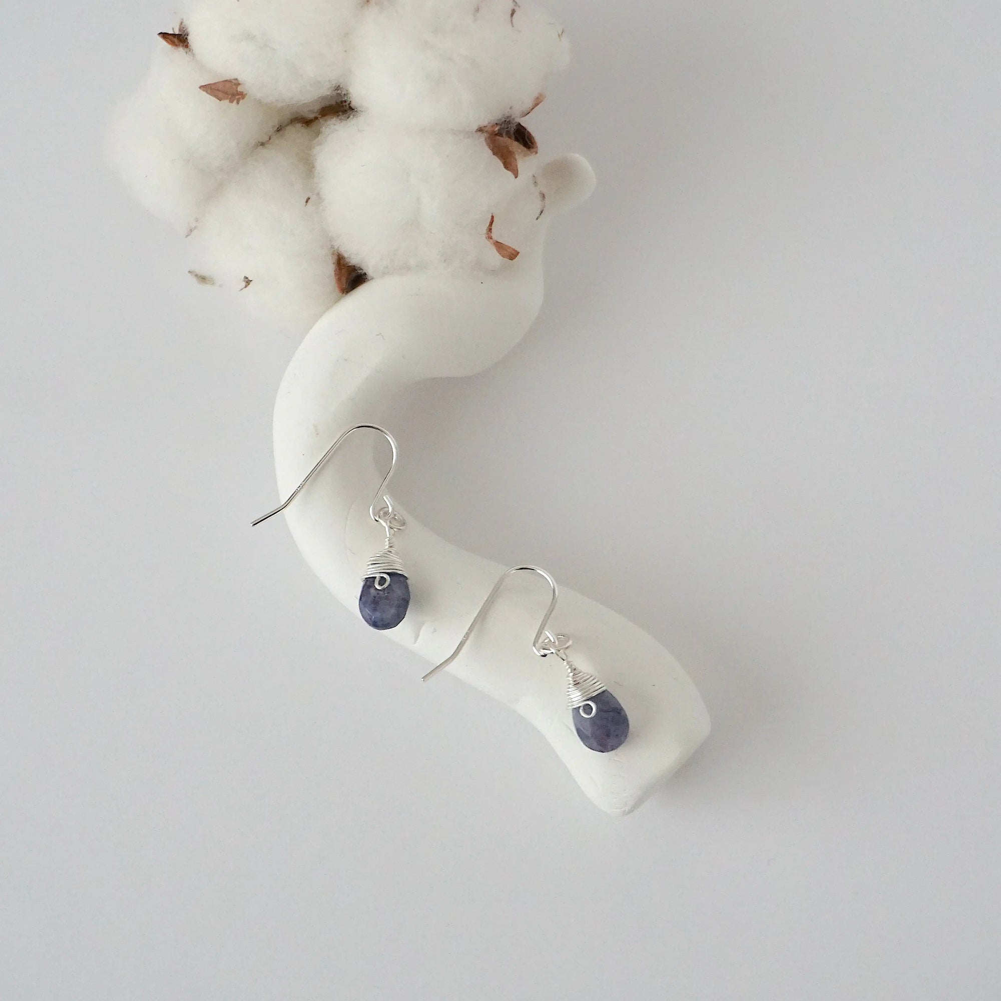 Sapphire sterling silver drop earrings with faceted natural sapphire stones and wire wrapping, laying flat on a display – Designs by Nature Gems