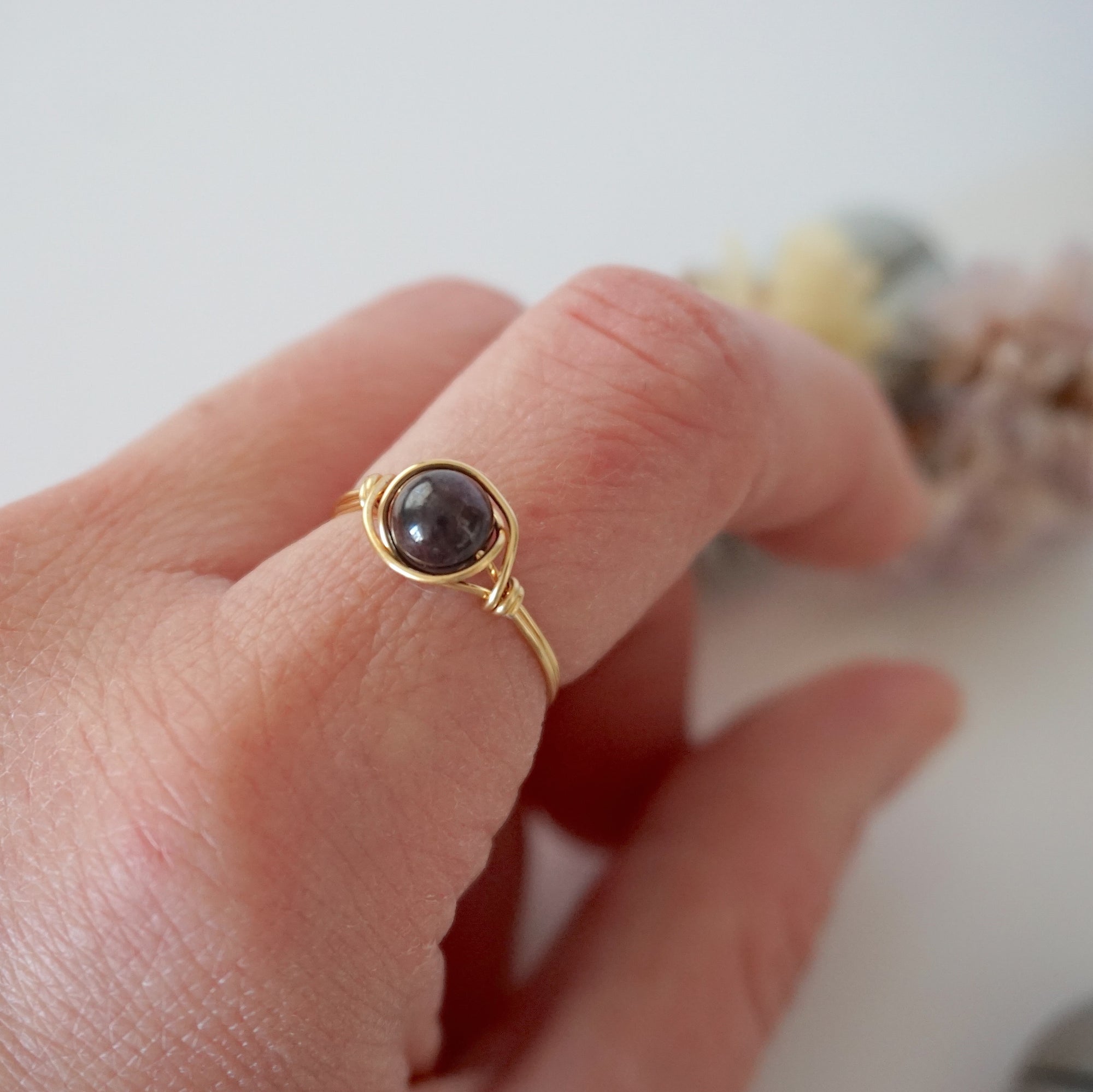 Simple garnet ring with polished garnet bead in minimalist gold wire wrap on woman’s hand
