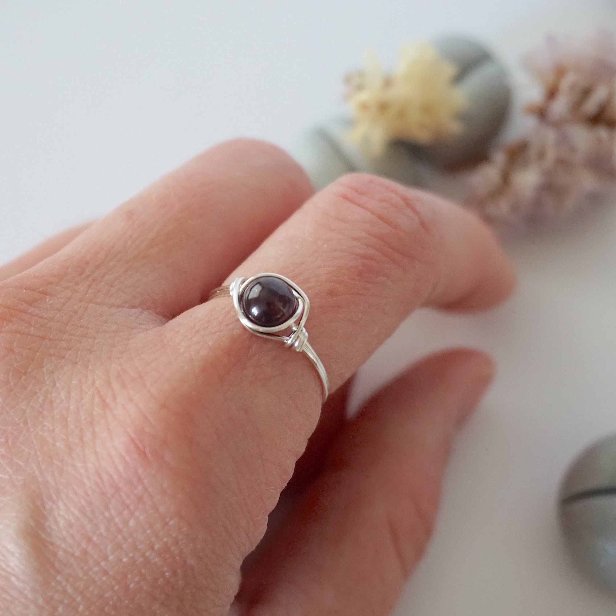 Minimalist garnet bead ring in silver wire wrap on woman’s hand, dainty January birthstone jewelry