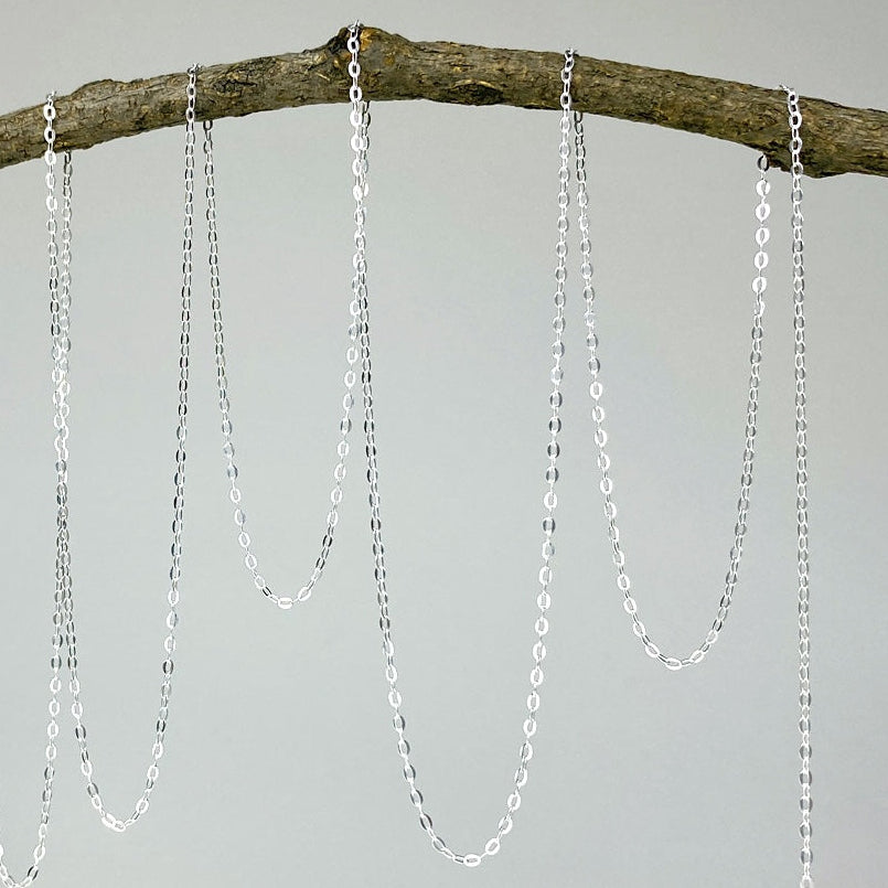 Silver chain necklaces hanging from a branch on a white background