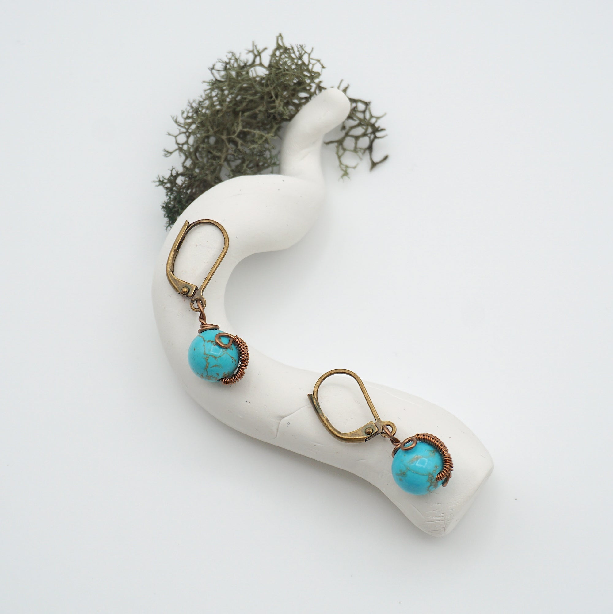 Bird’s eye view of turquoise drop earrings laying flat on a display, showing detailed wire wrapping and gemstone color.